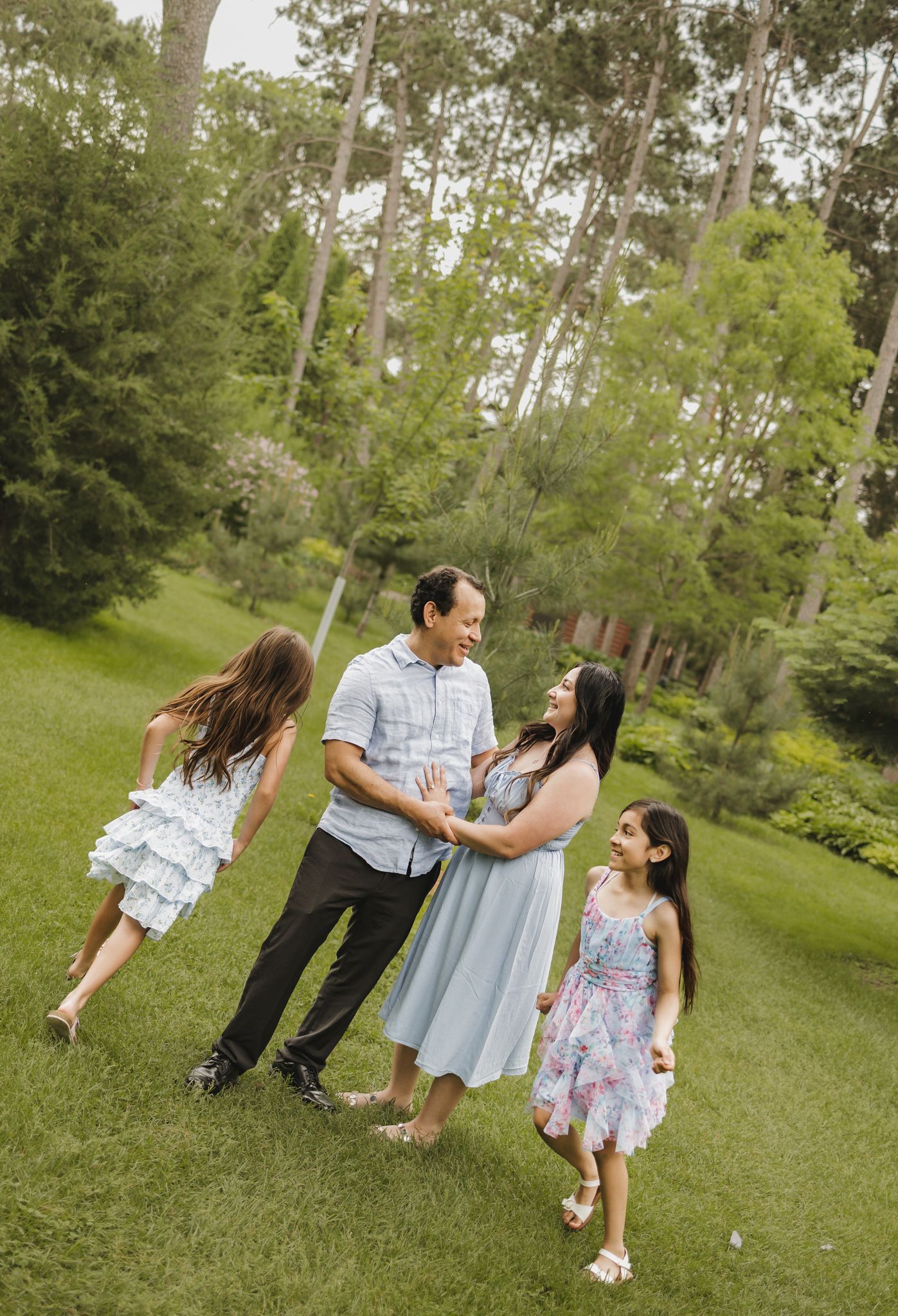 Happy family of four laughing and playing together on lush green grass in a wooded park setting.