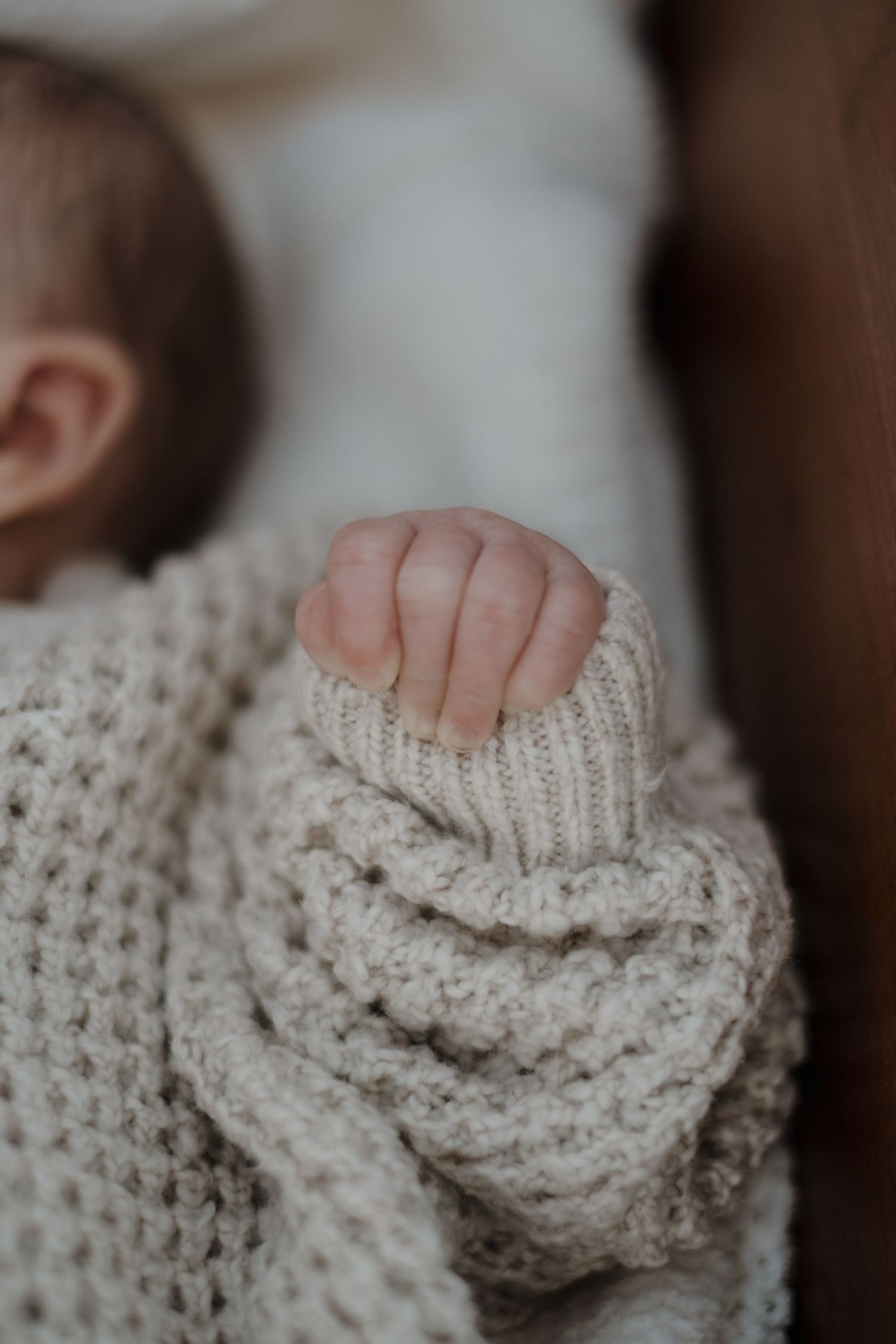 Extreme close-up of tiny fingers grasping cream colored knit fabric.