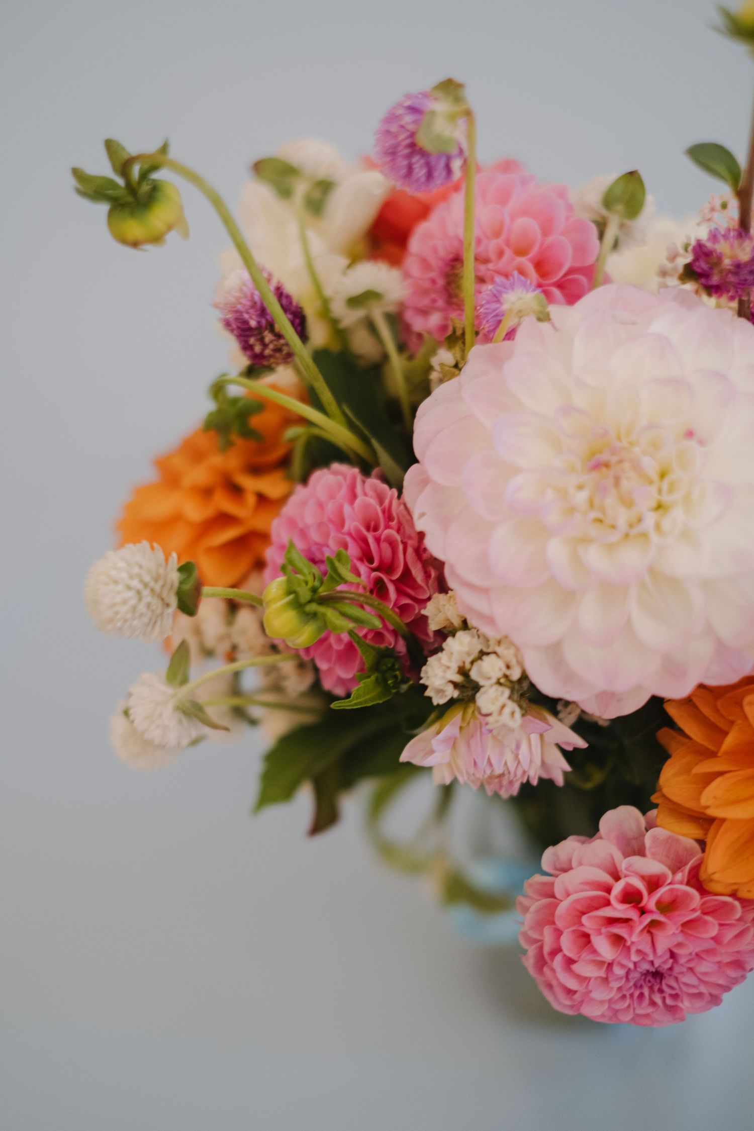 Delicate pink and orange floral arrangement with dahlias and mixed flowers against a soft blurred background.