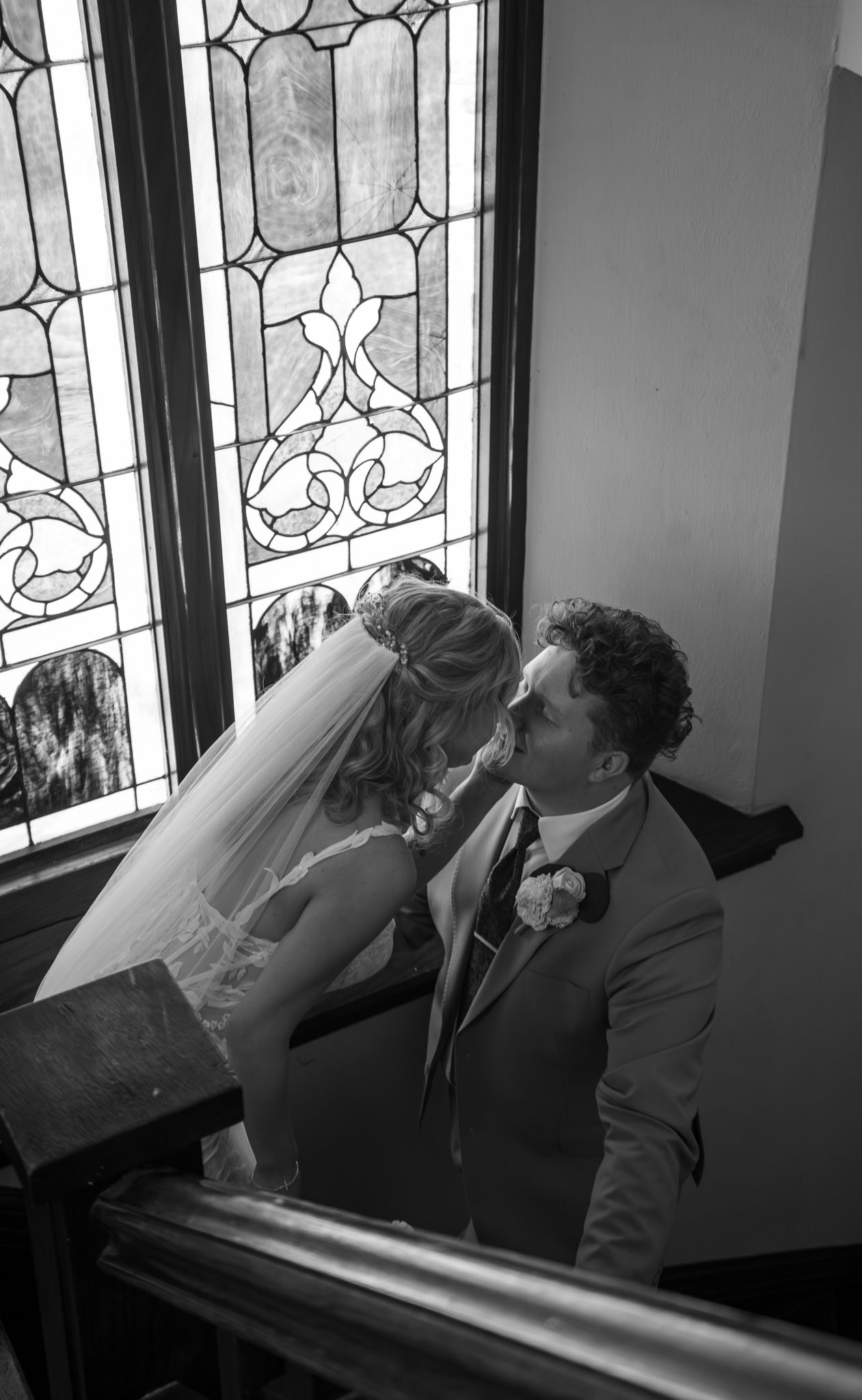 A tender wedding moment by stained glass windows as the couple shares an intimate kiss.
