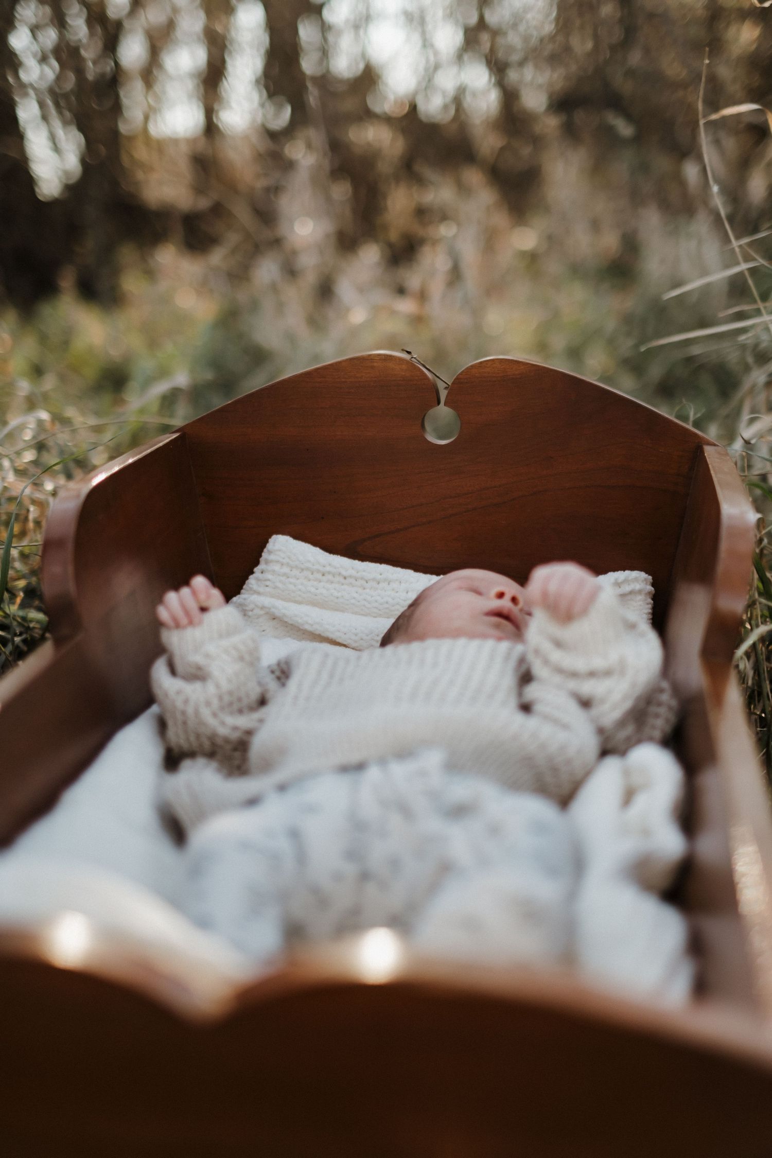 Newborn baby sleeping peacefully in white knit clothing on wooden antique cradle.