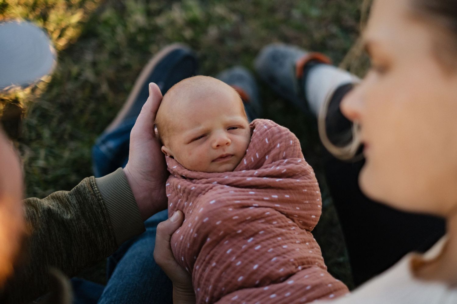 Smiling baby wrapped in a dusty rose blanket being held outdoors.