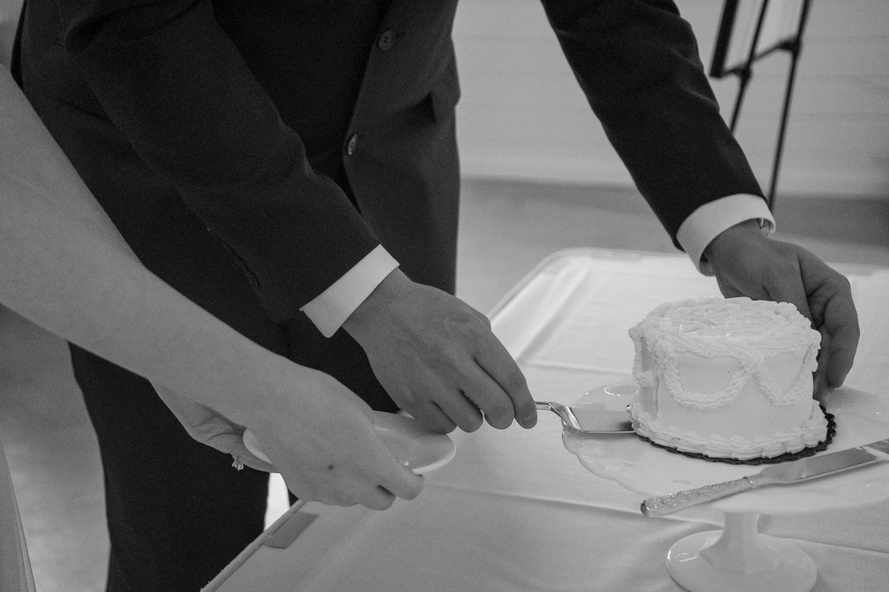 Hands cutting into a white wedding cake at a reception.