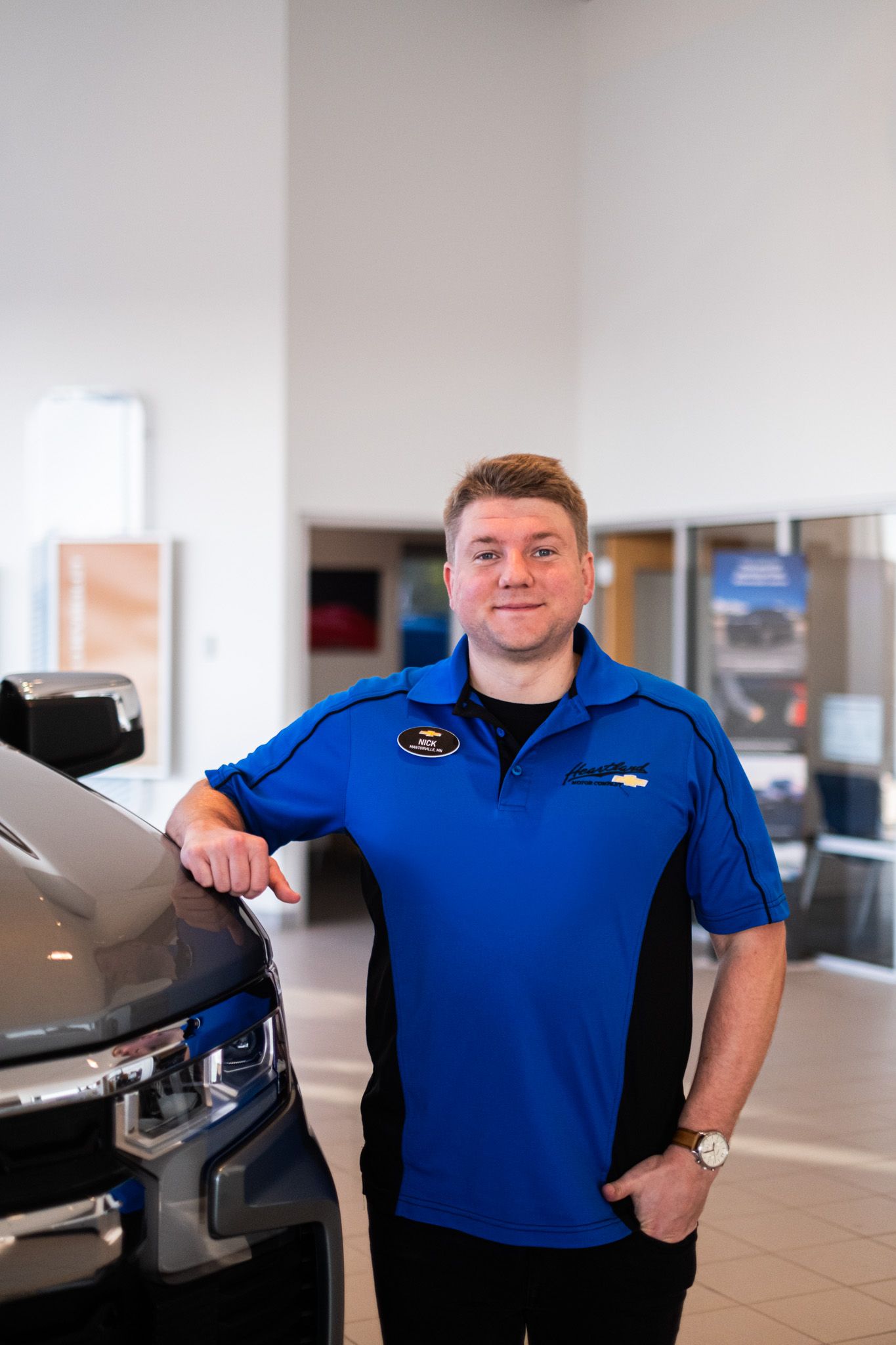 Automotive dealership employee in blue polo shirt posing next to vehicle in showroom.