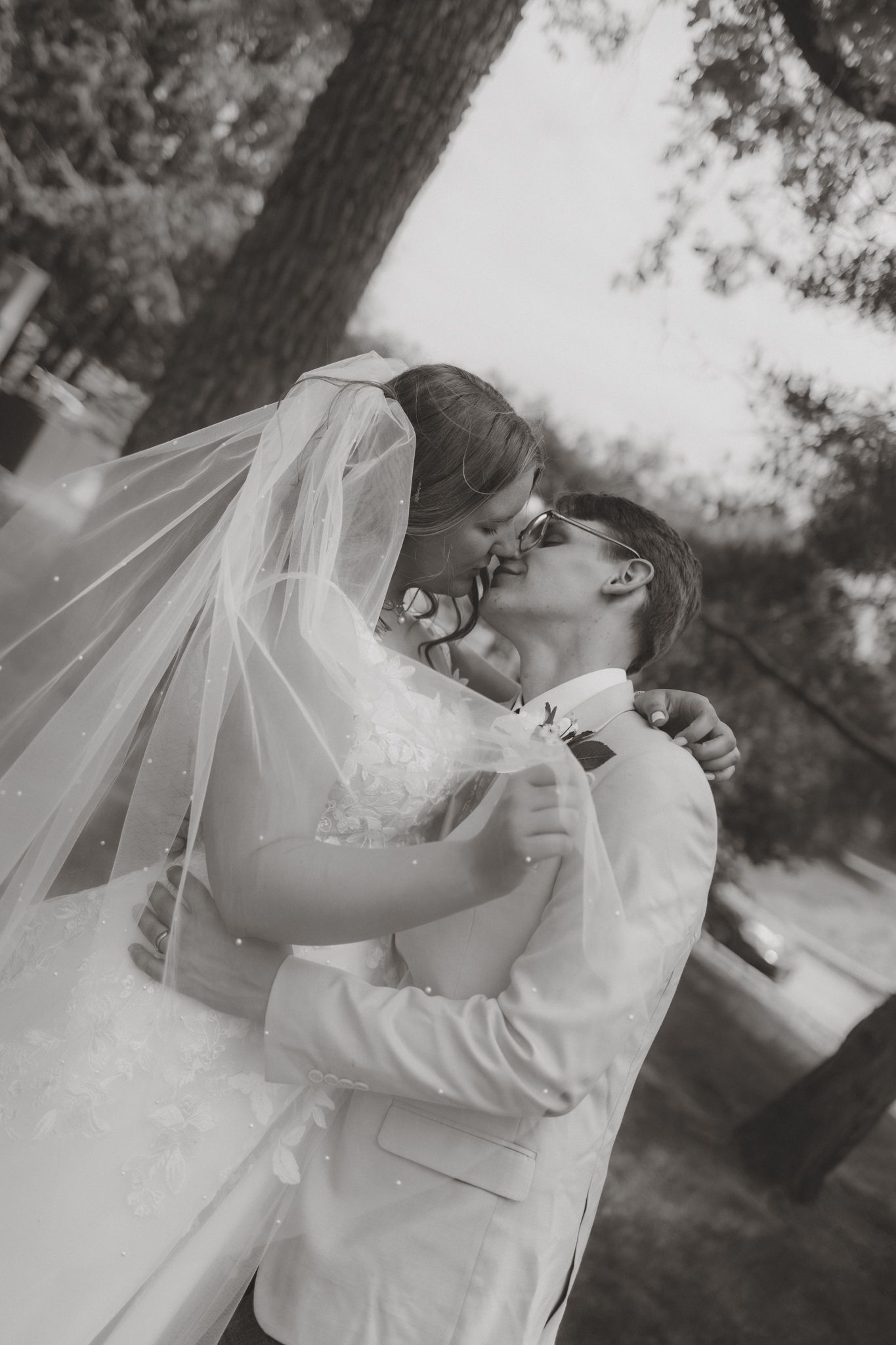Black and white photo of bride and groom sharing a romantic kiss outdoors on their wedding day.