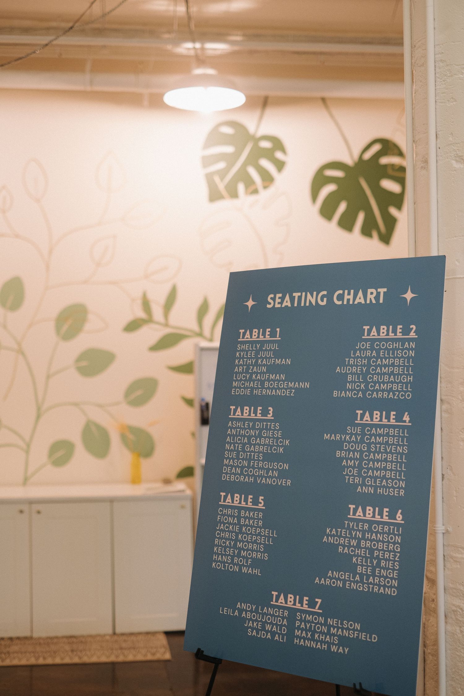 Wedding seating chart displayed on blue boards with white text listing table assignments.