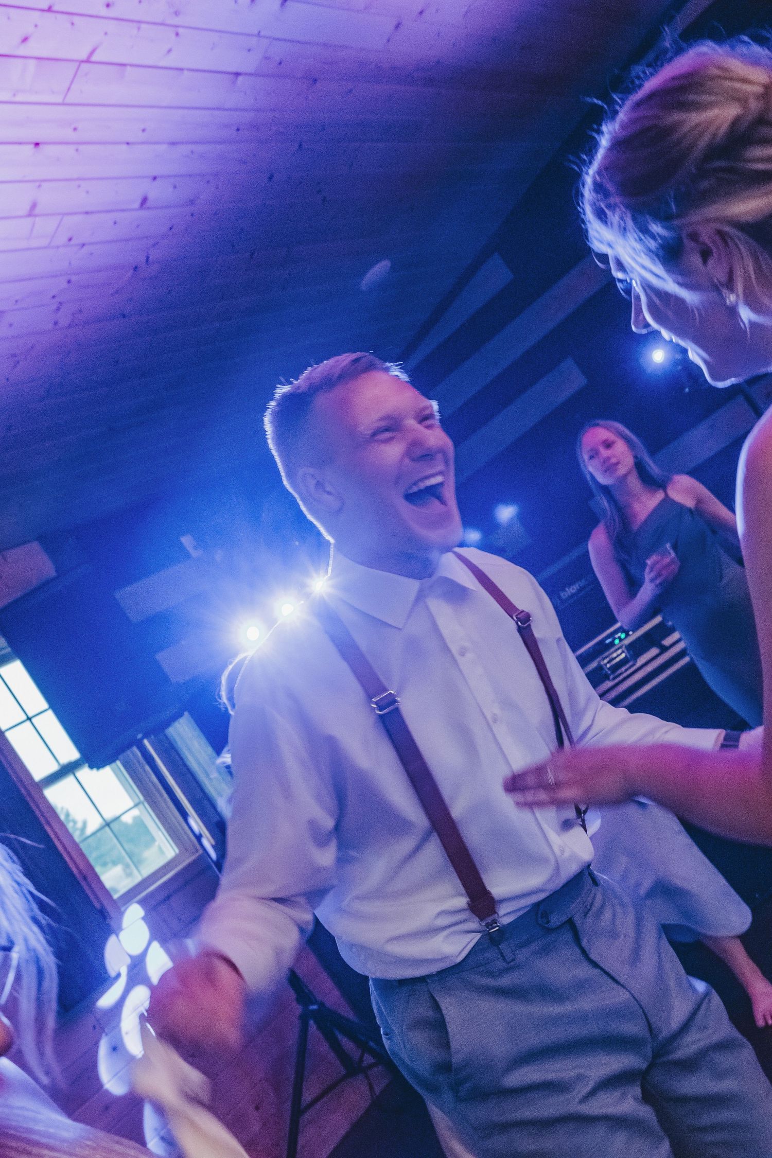 Joyful groom in white shirt and suspenders dancing at wedding reception.