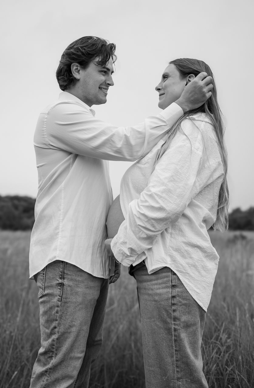 A black and white portrait of a couple sharing an intimate moment in a grassy field.