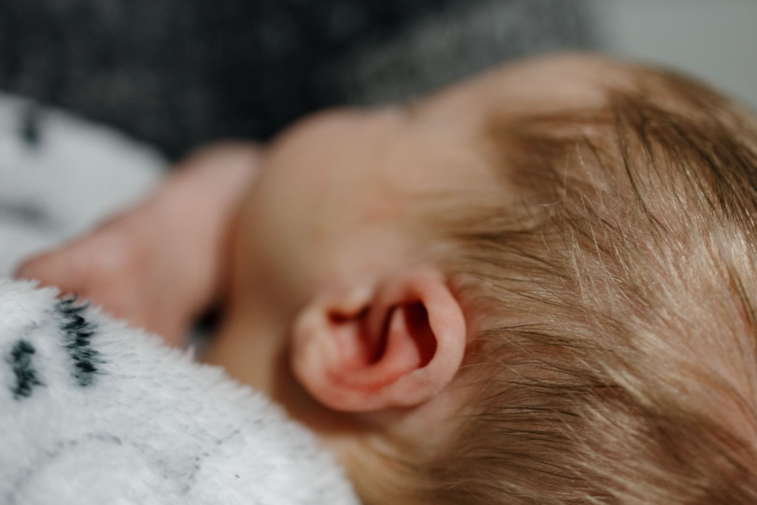 Close-up detail of a baby's ear and soft hair against white fabric.