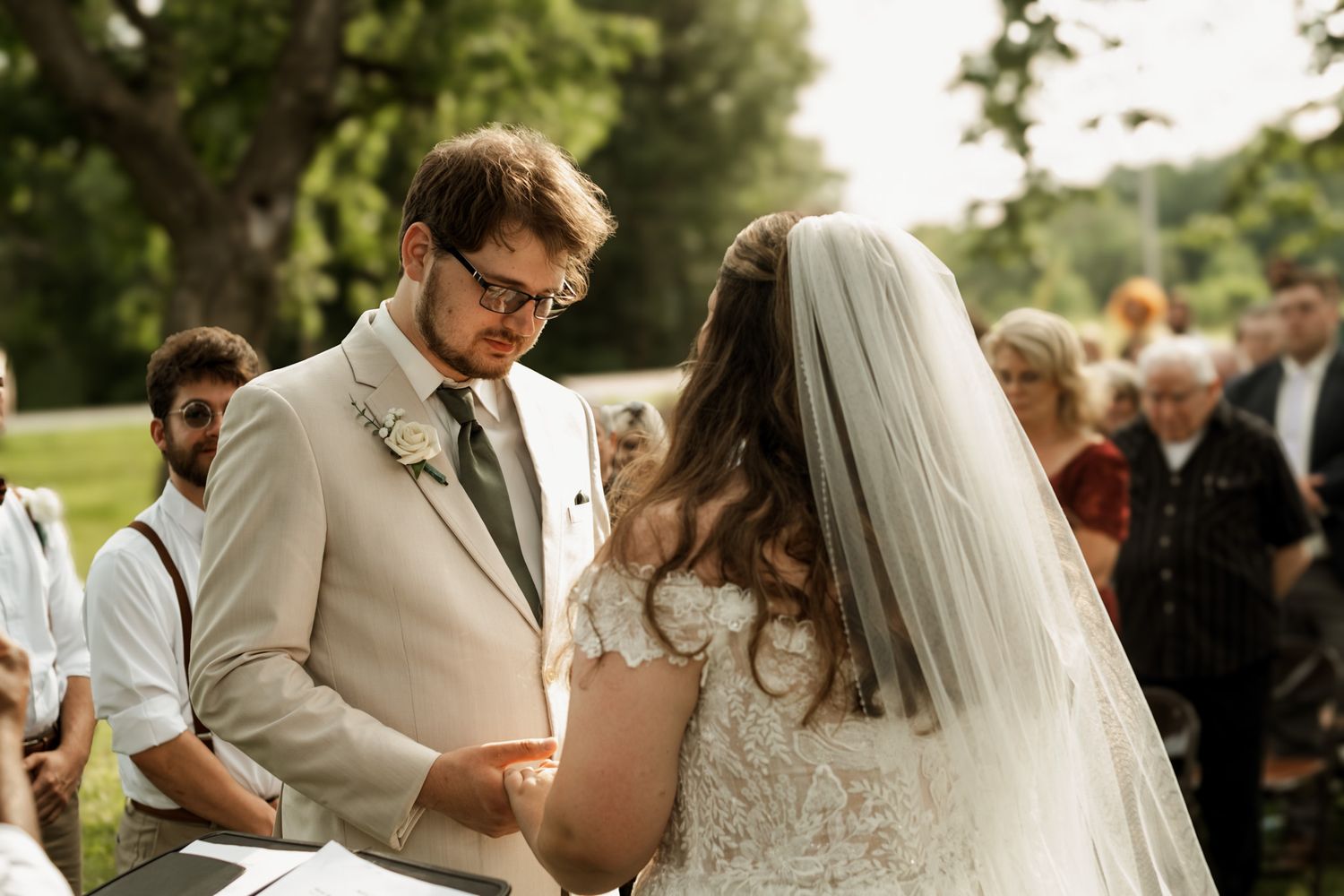 Outdoor wedding ceremony with guests seated on lawn watching couple exchange vows.