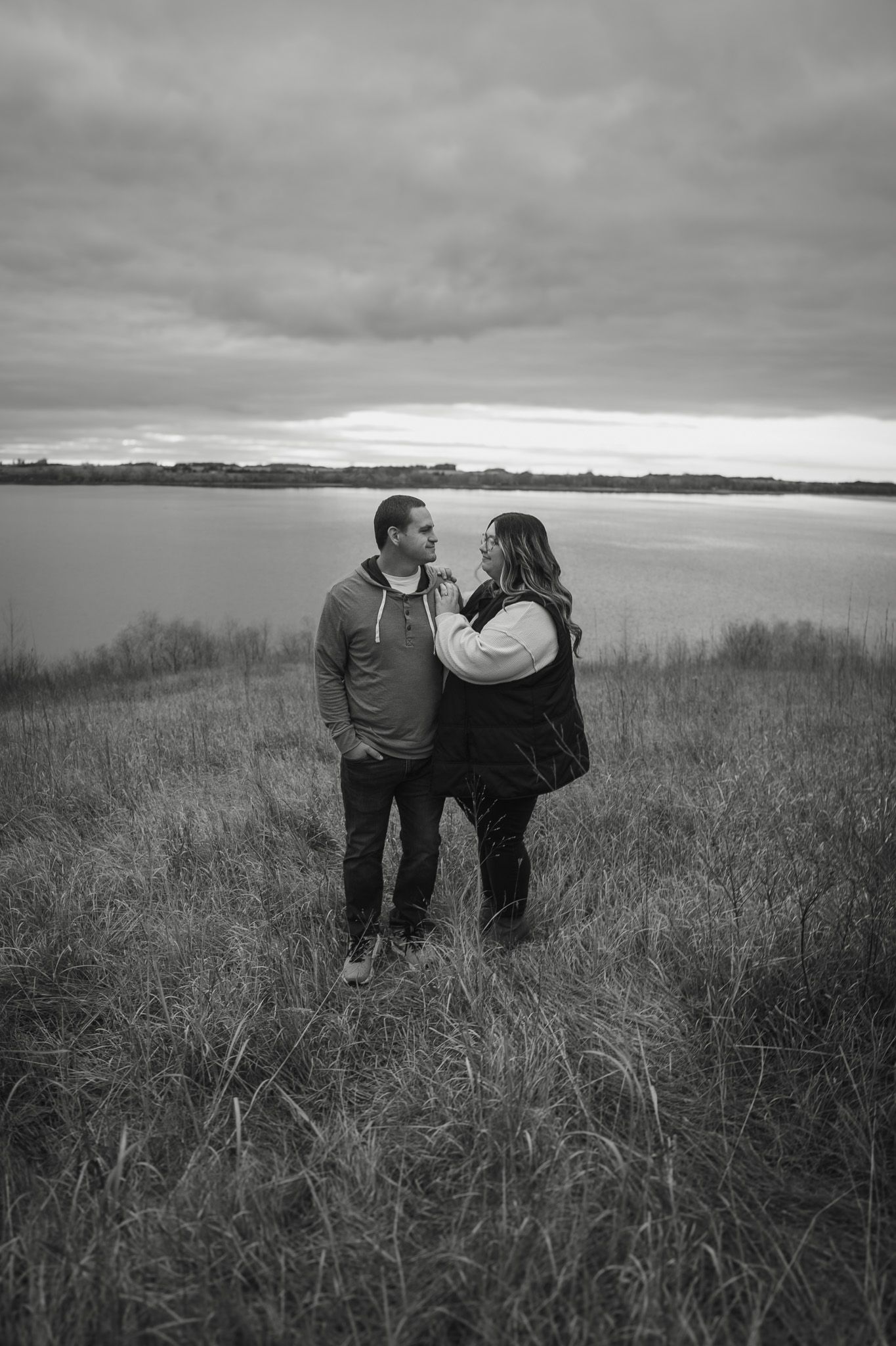 A couple stands together in a misty field during golden hour.