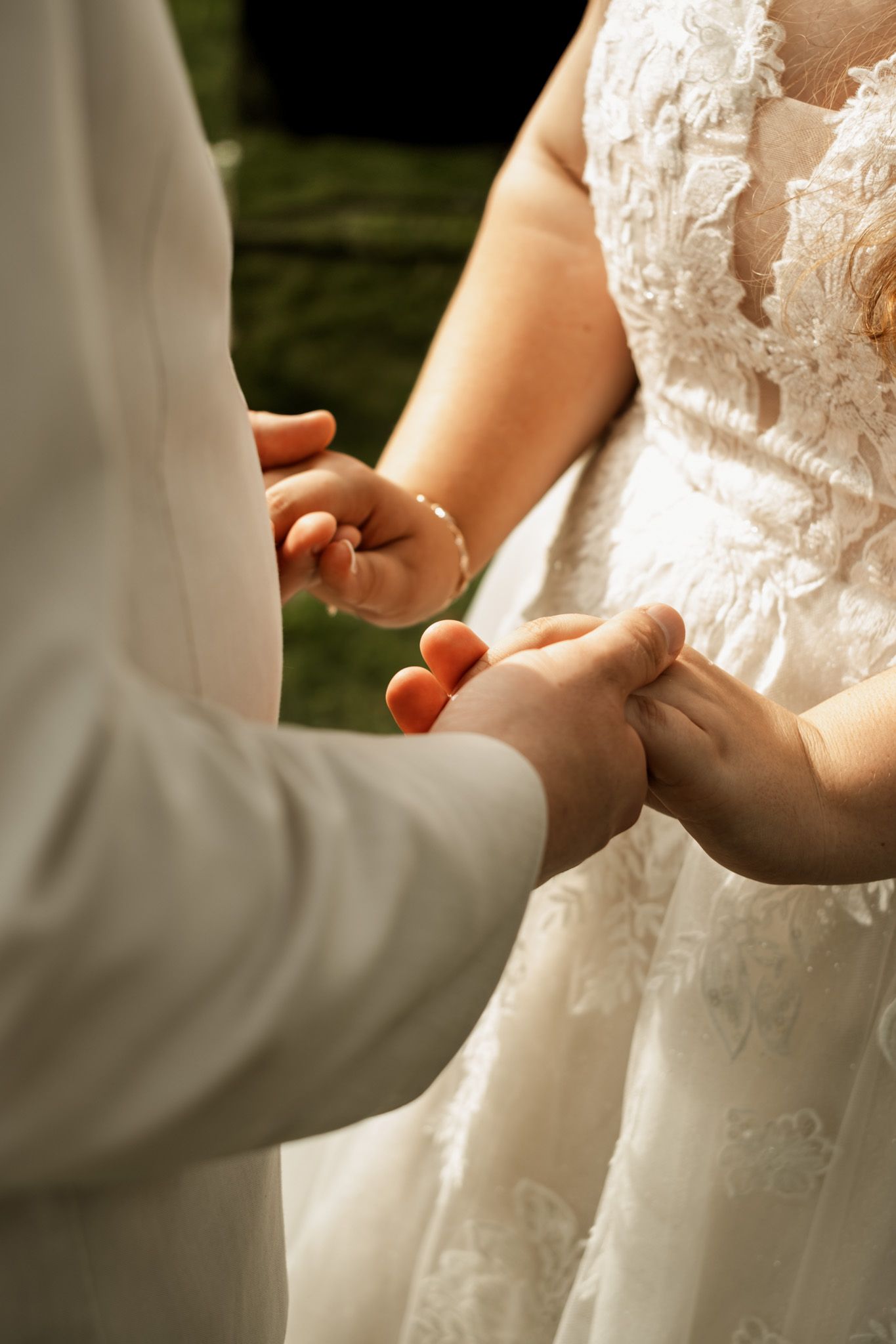 Close-up of hands during ring exchange at outdoor wedding ceremony.