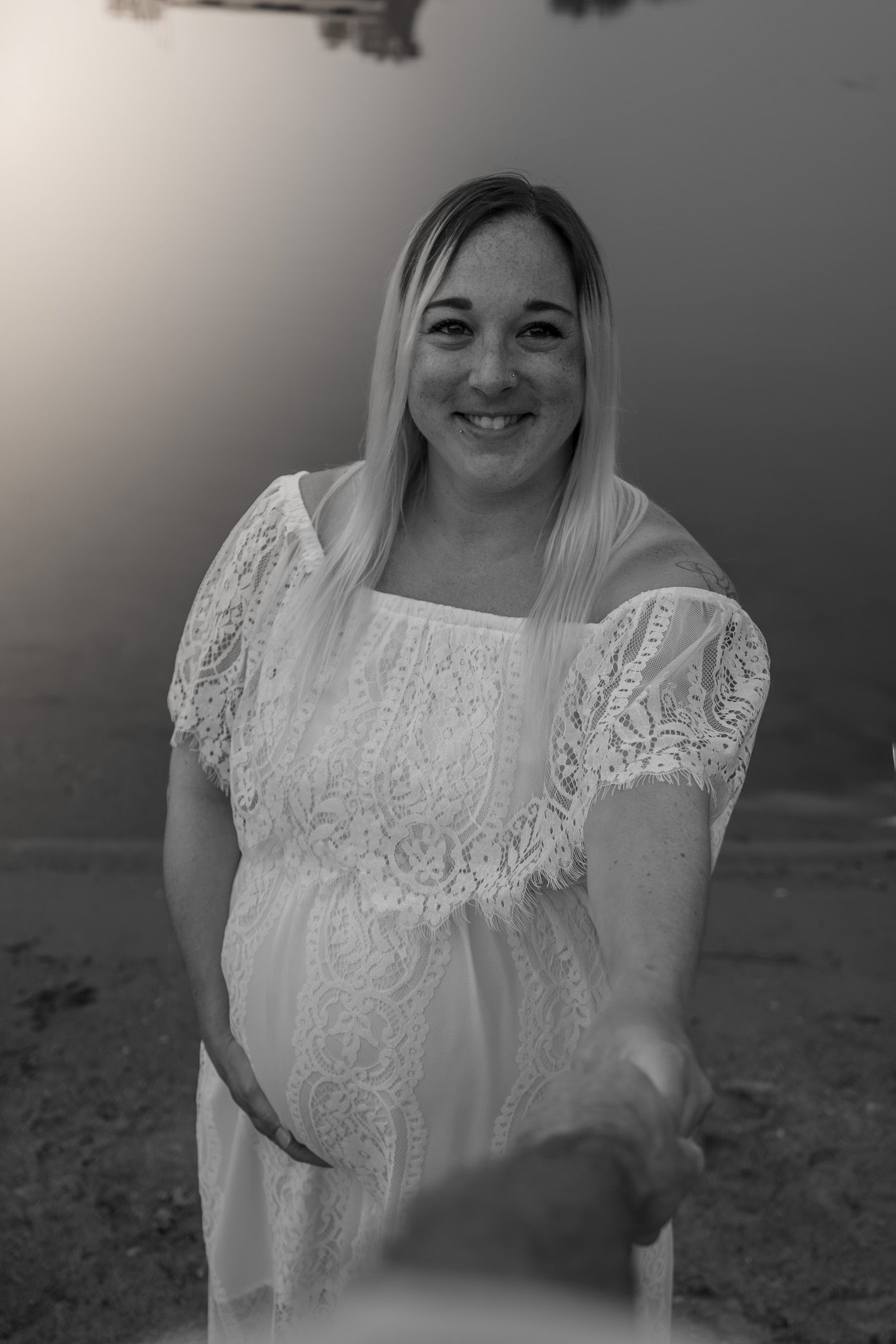 An artistic black and white portrait of an expectant mother wearing a lace dress outdoors.