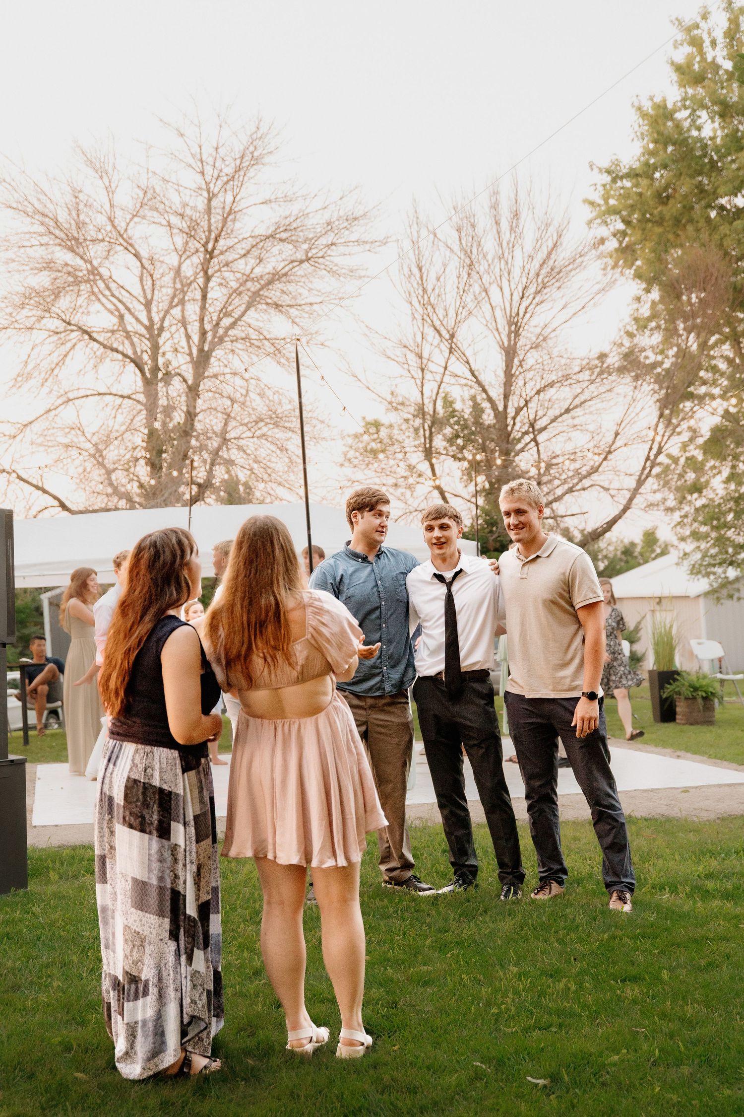 Wedding guests mingle and socialize on a green lawn during an outdoor evening wedding reception celebration.