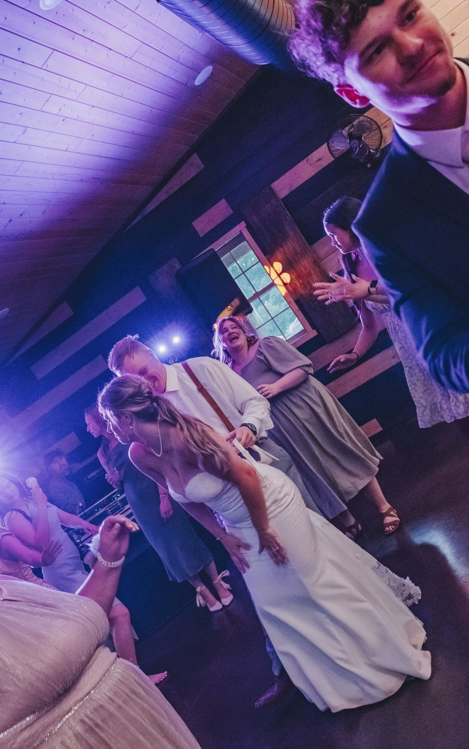 Bride laughing and dancing with guests at rustic wedding reception venue.