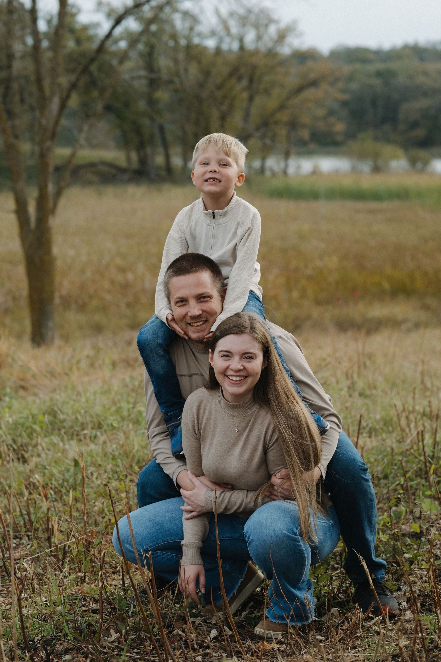 Playful couple poses together in a grassy autumn field during a casual outdoor photoshoot.