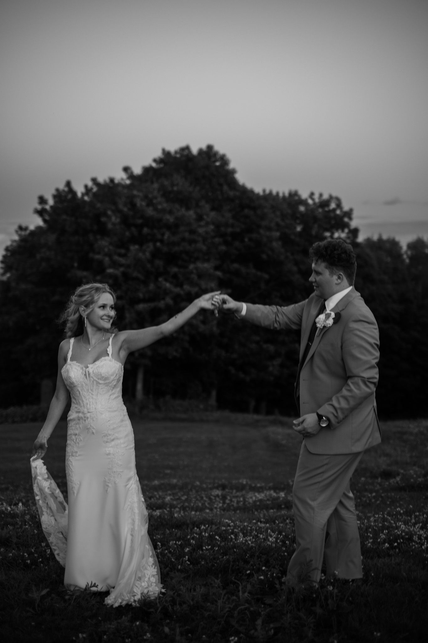 Couple dancing playfully in a field at sunset in black and white.