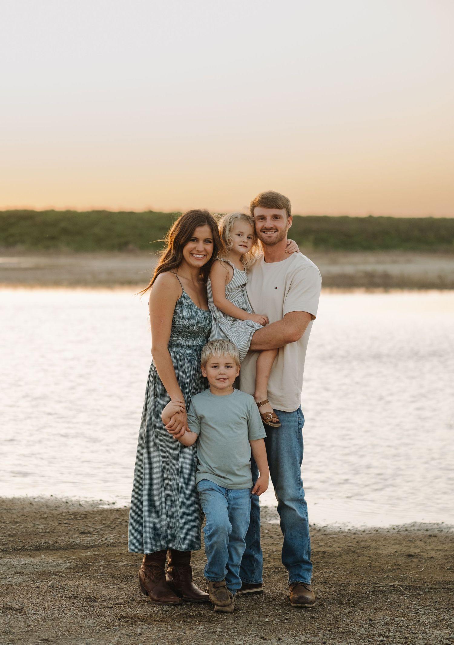 A family of four poses together at sunset on a beach with water in the background.