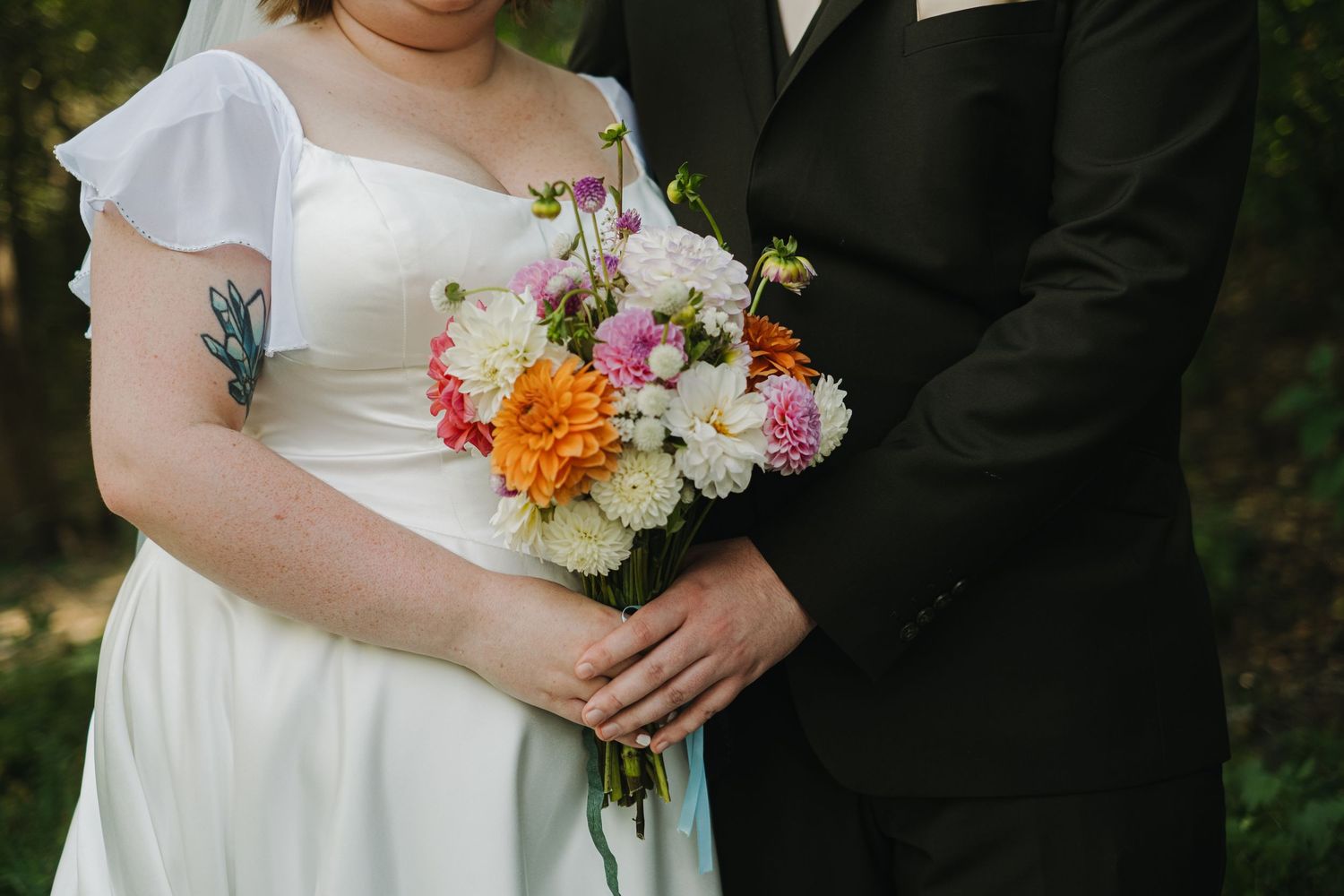 Wedding couple embracing outdoors with colorful floral bouquet details.
