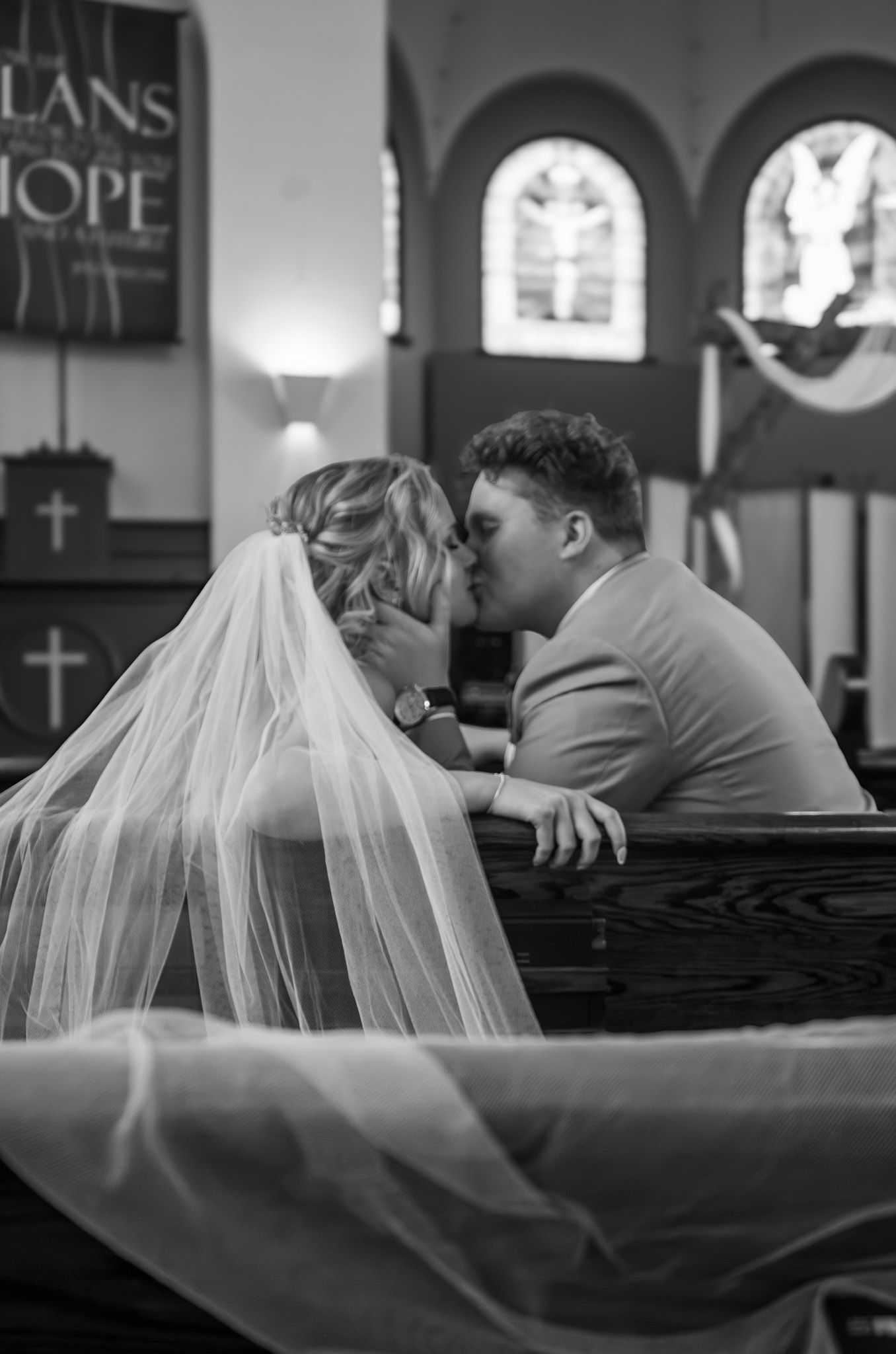 A romantic wedding moment captured in black and white as the couple shares a kiss in church pews.