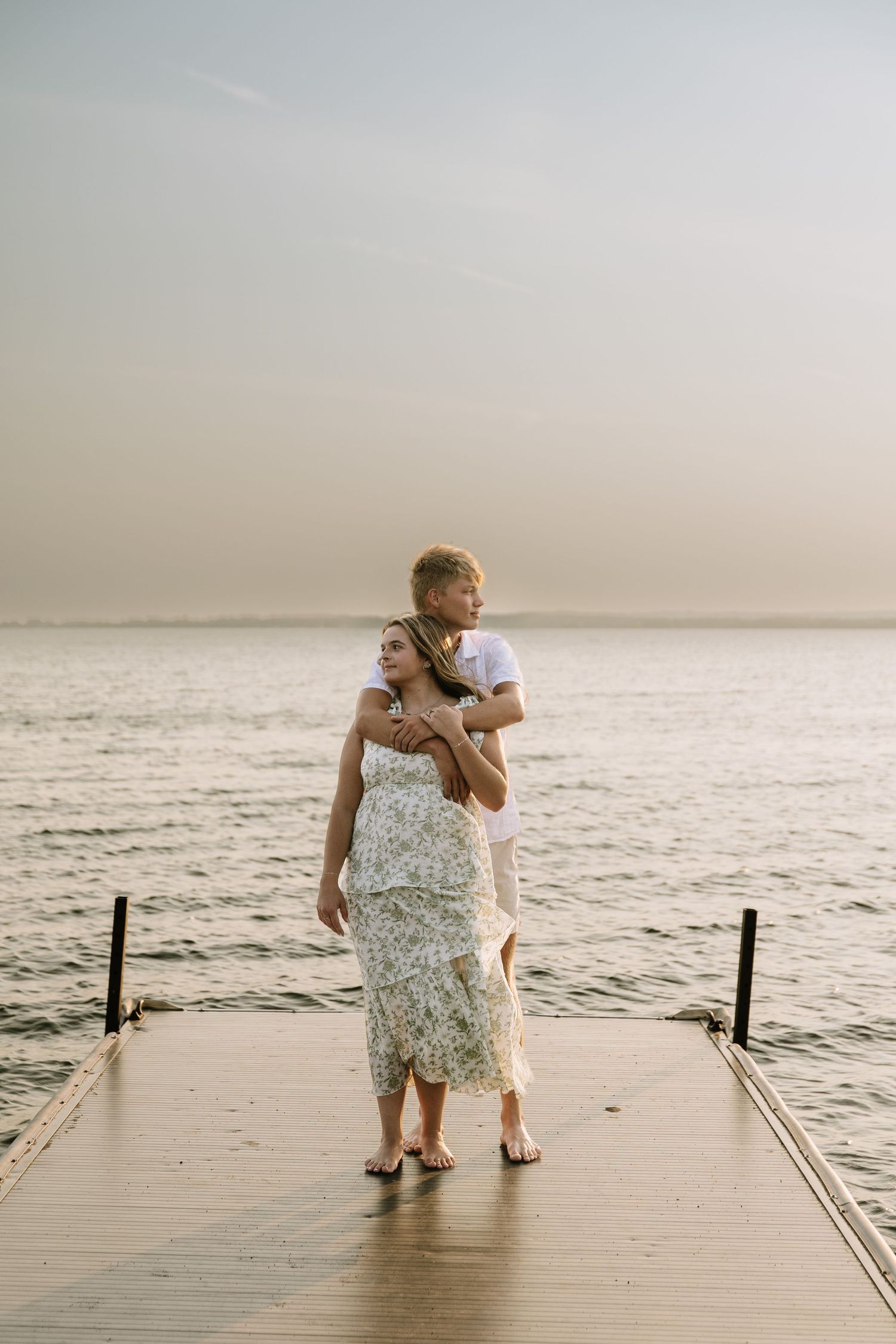 Couple embracing on a wooden pier at sunset with calm ocean waters in the background.