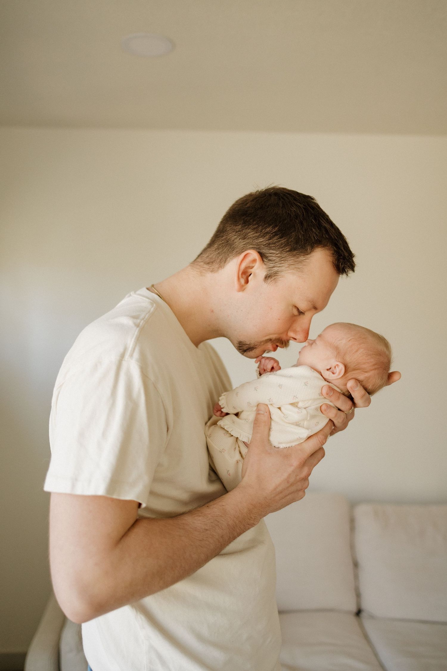 A father tenderly kisses his swaddled newborn baby while holding them close in a bright, cozy room.