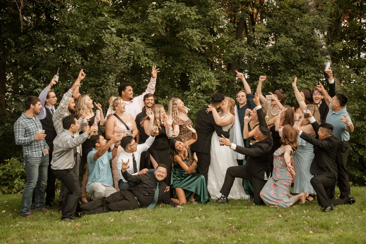 Large group of wedding guests jumping and celebrating outdoors in a fun group photo.