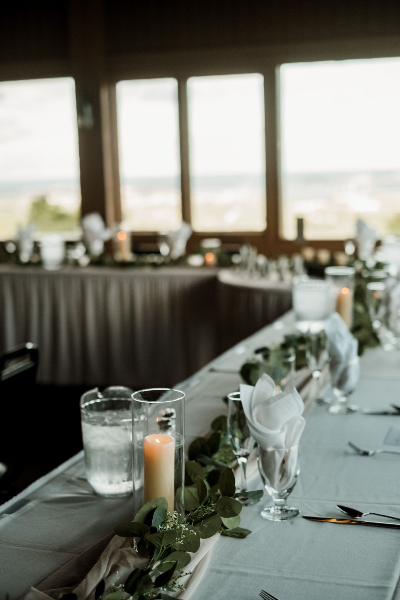 Elegant wedding reception table setup with white linens and greenery centerpieces.