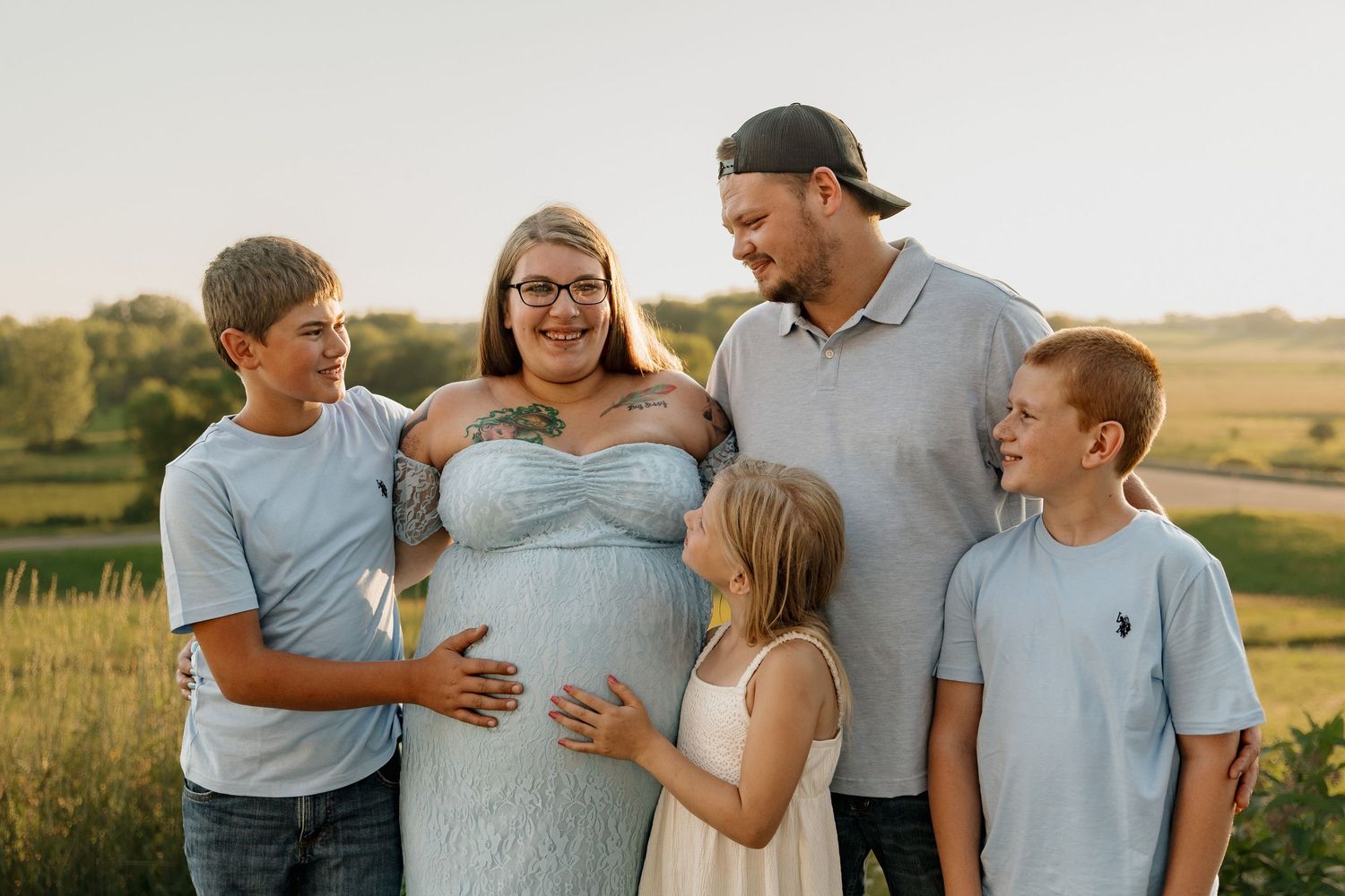 Pregnant woman poses outdoors with her husband and three children during a golden hour family maternity photo session.