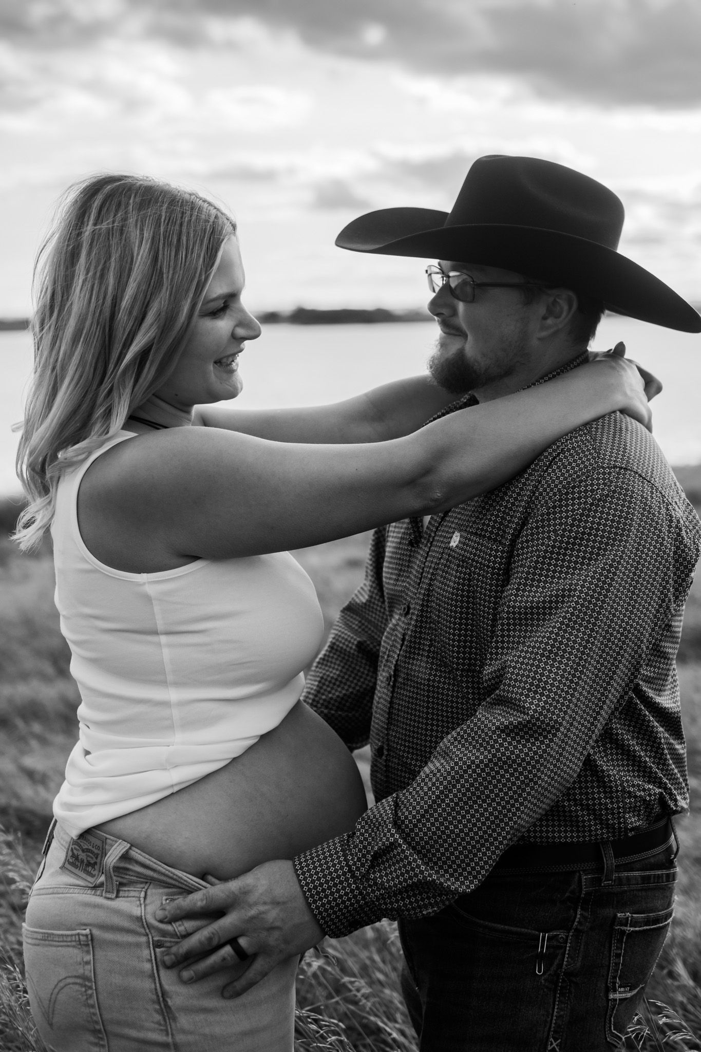 A couple embraces in a field during a romantic maternity photoshoot.