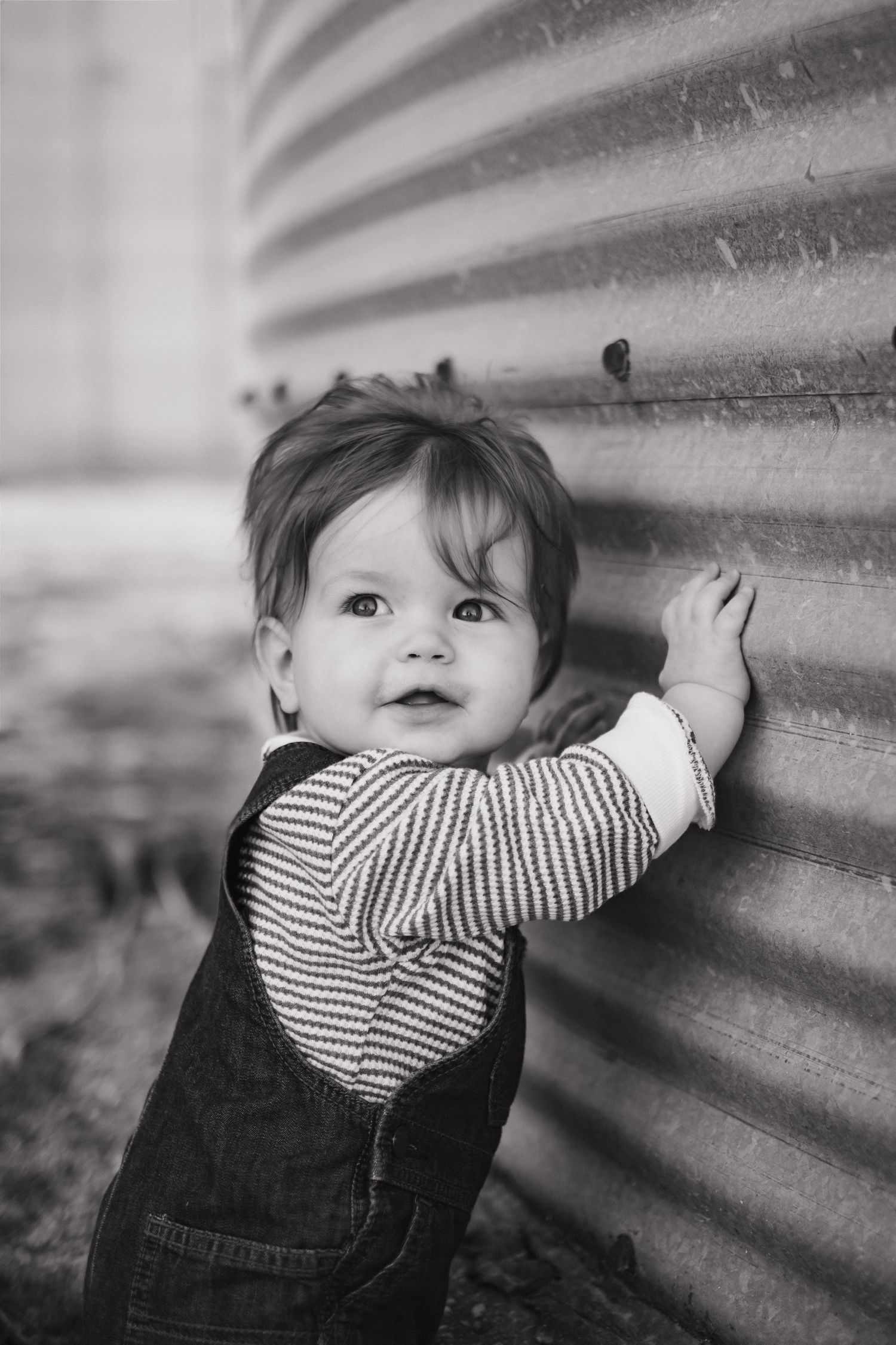 Black and white series of a small child peeking through metal siding with playful expressions.