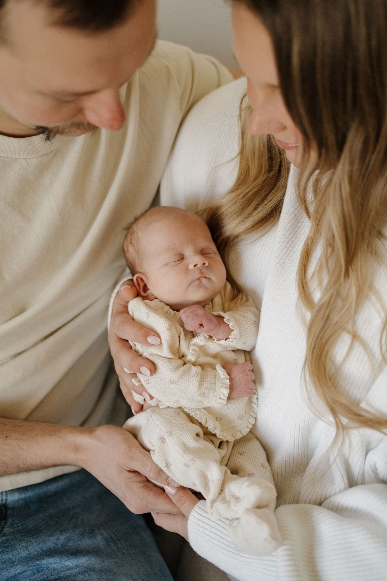 Parents tenderly holding their sleeping newborn baby dressed in a cream outfit during a lifestyle newborn photo session.