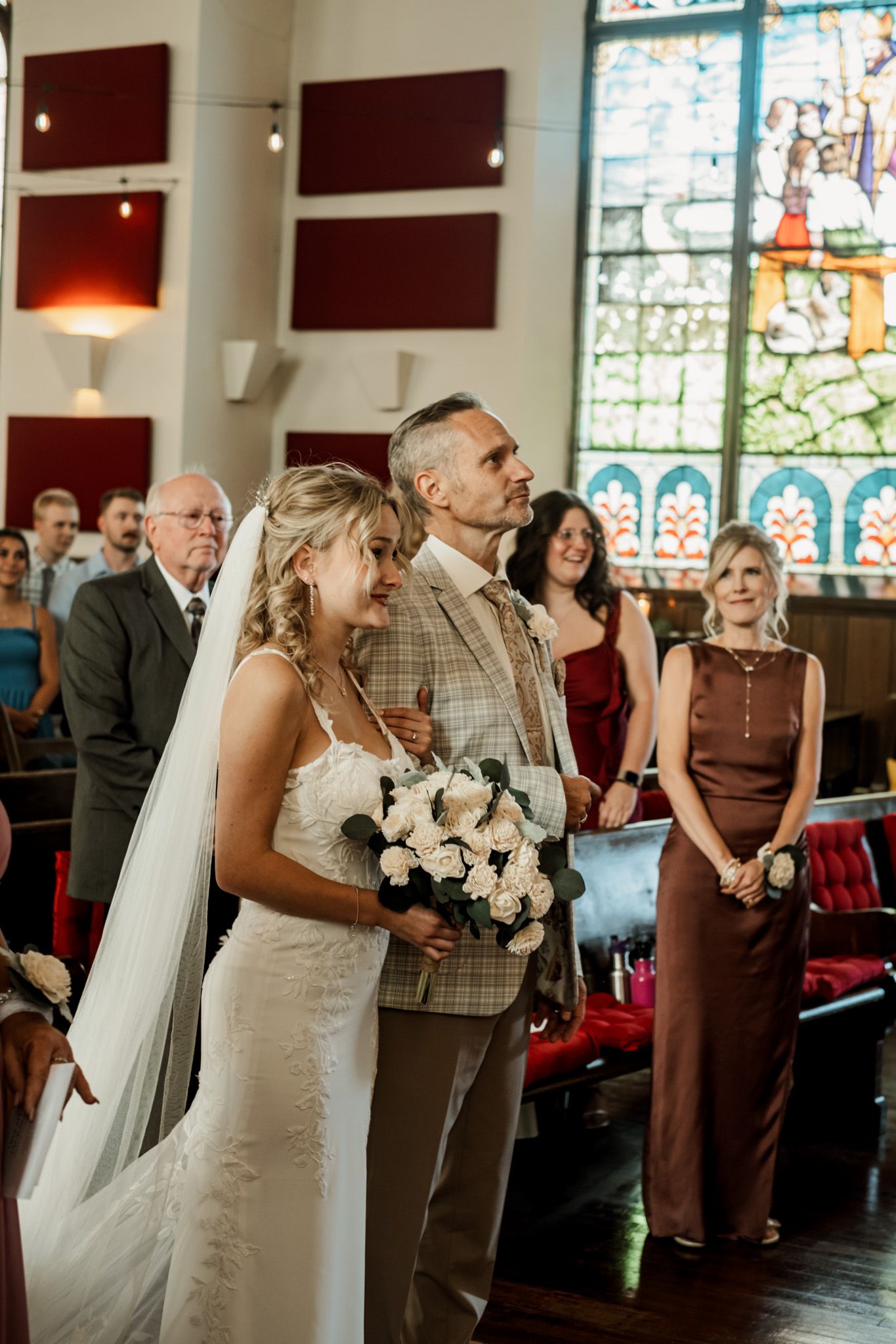Wedding ceremony in church with stained glass windows and burgundy interior decor.