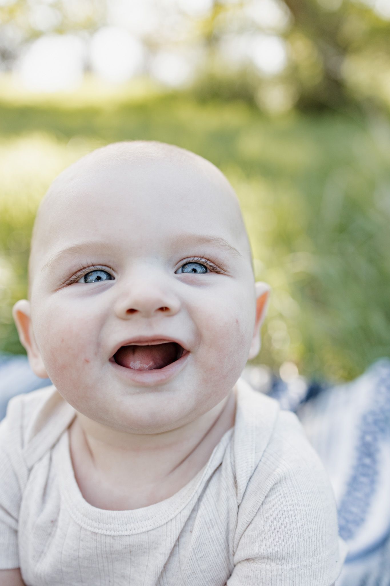Happy smiling baby with blue eyes lying on blanket outdoors in natural green setting.