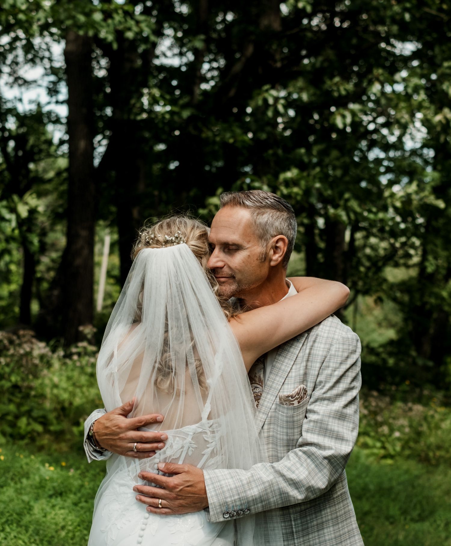 Emotional first look moment between bride and father in a lush green outdoor setting.