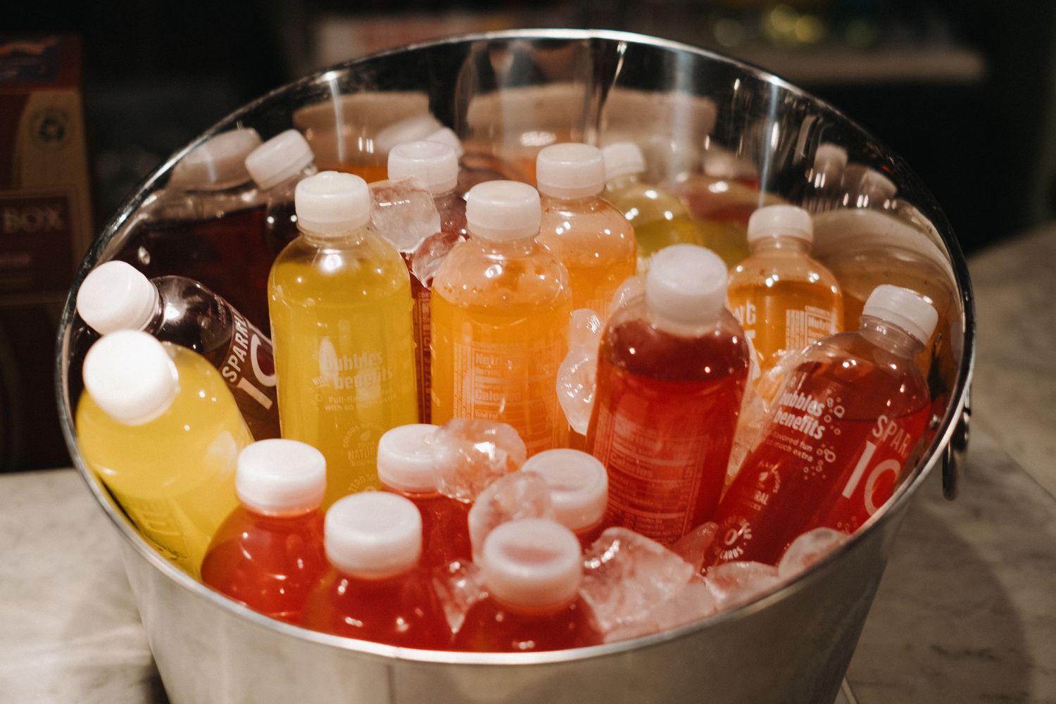 Colorful cocktail mixers and bottles chilling in an ice bucket.