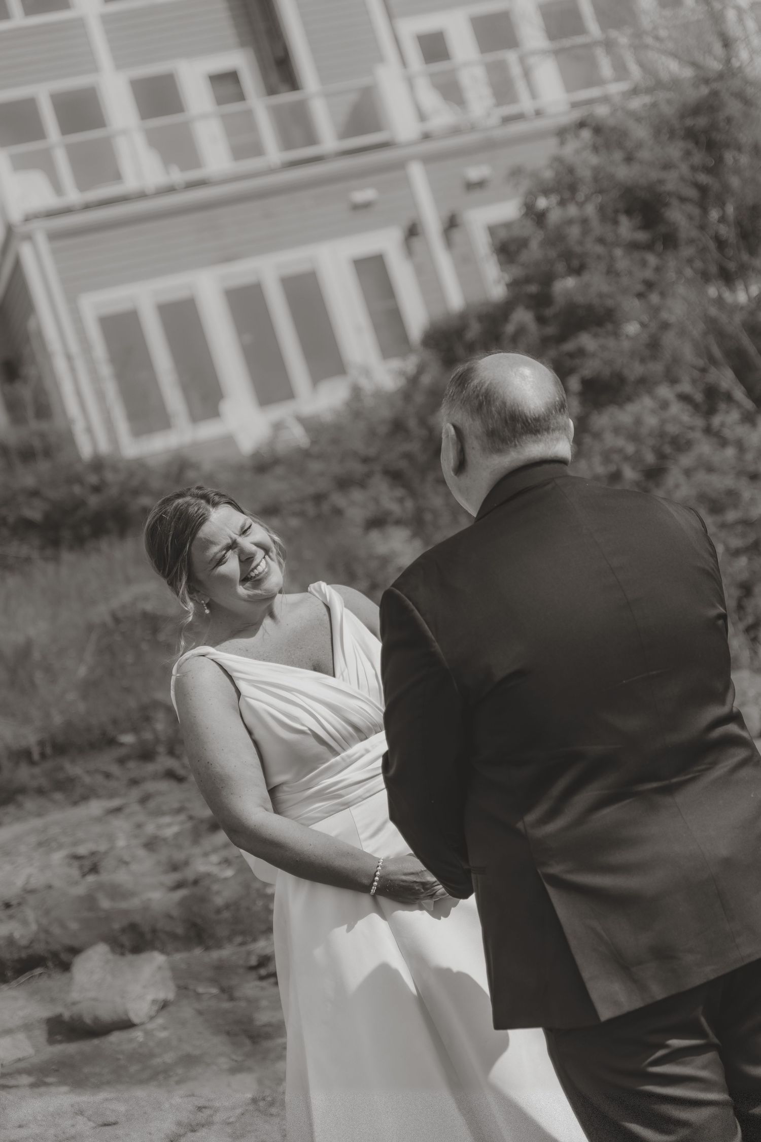 Bride laughing joyfully while holding hands with groom during outdoor wedding ceremony.