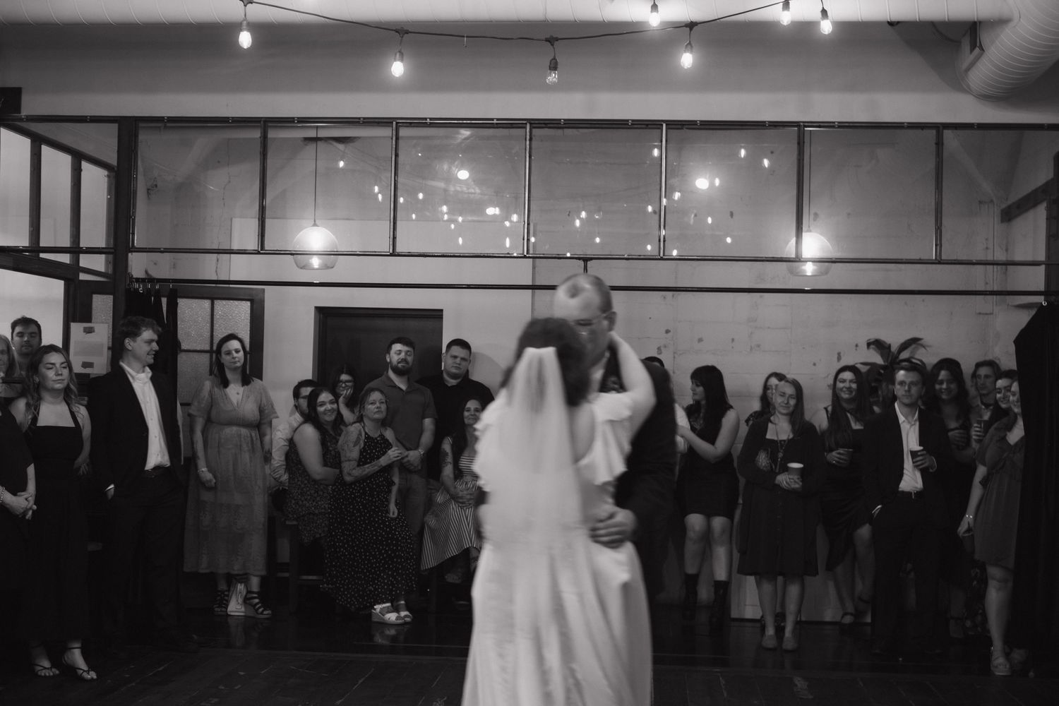 Wide view of an illuminated event space with guests gathered along the walls.