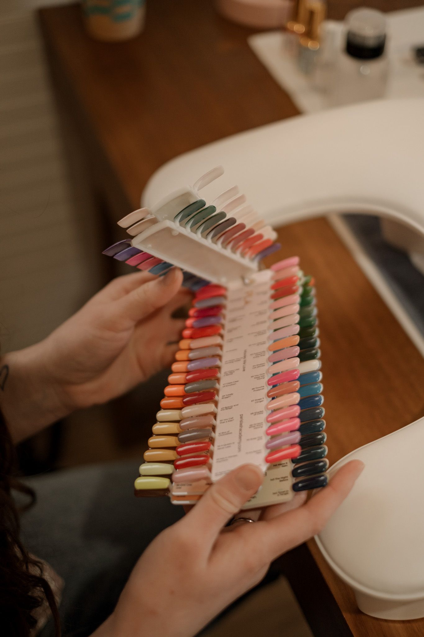 Hands holding nail polish color swatches in various shades arranged in a fan pattern.