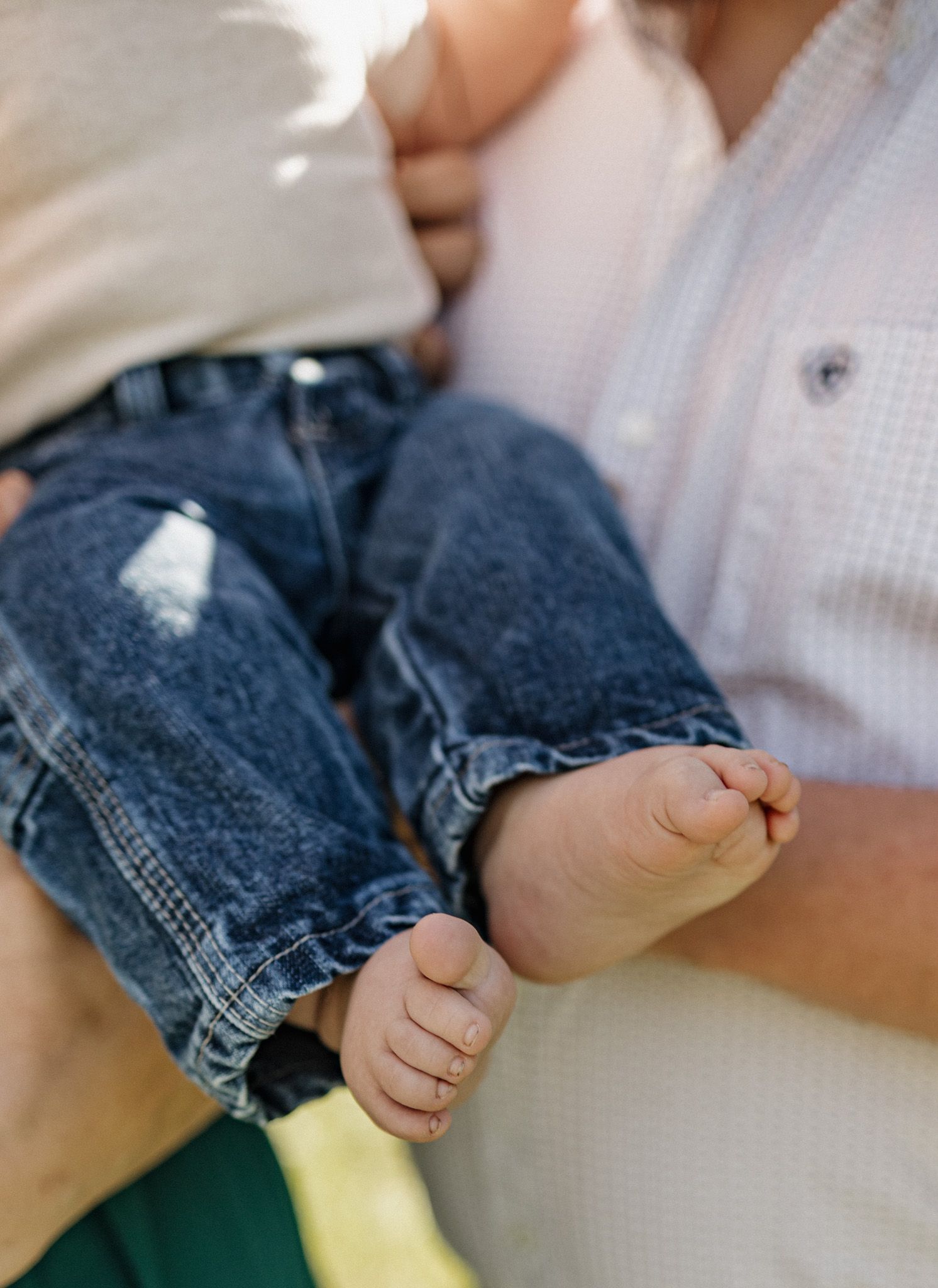 Close-up of a baby's bare feet and tiny toes while being held by an adult in a white shirt.