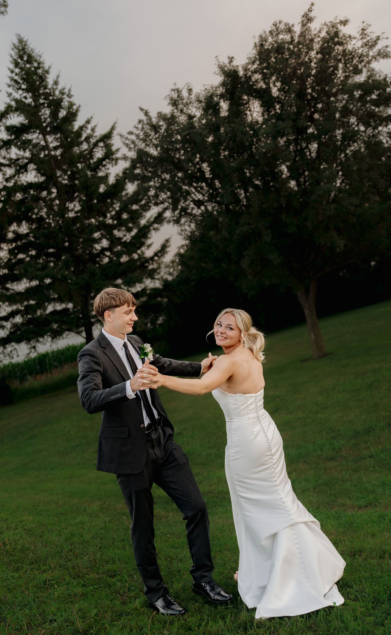 Bride and groom dancing outdoors on green lawn at sunset in wedding attire.