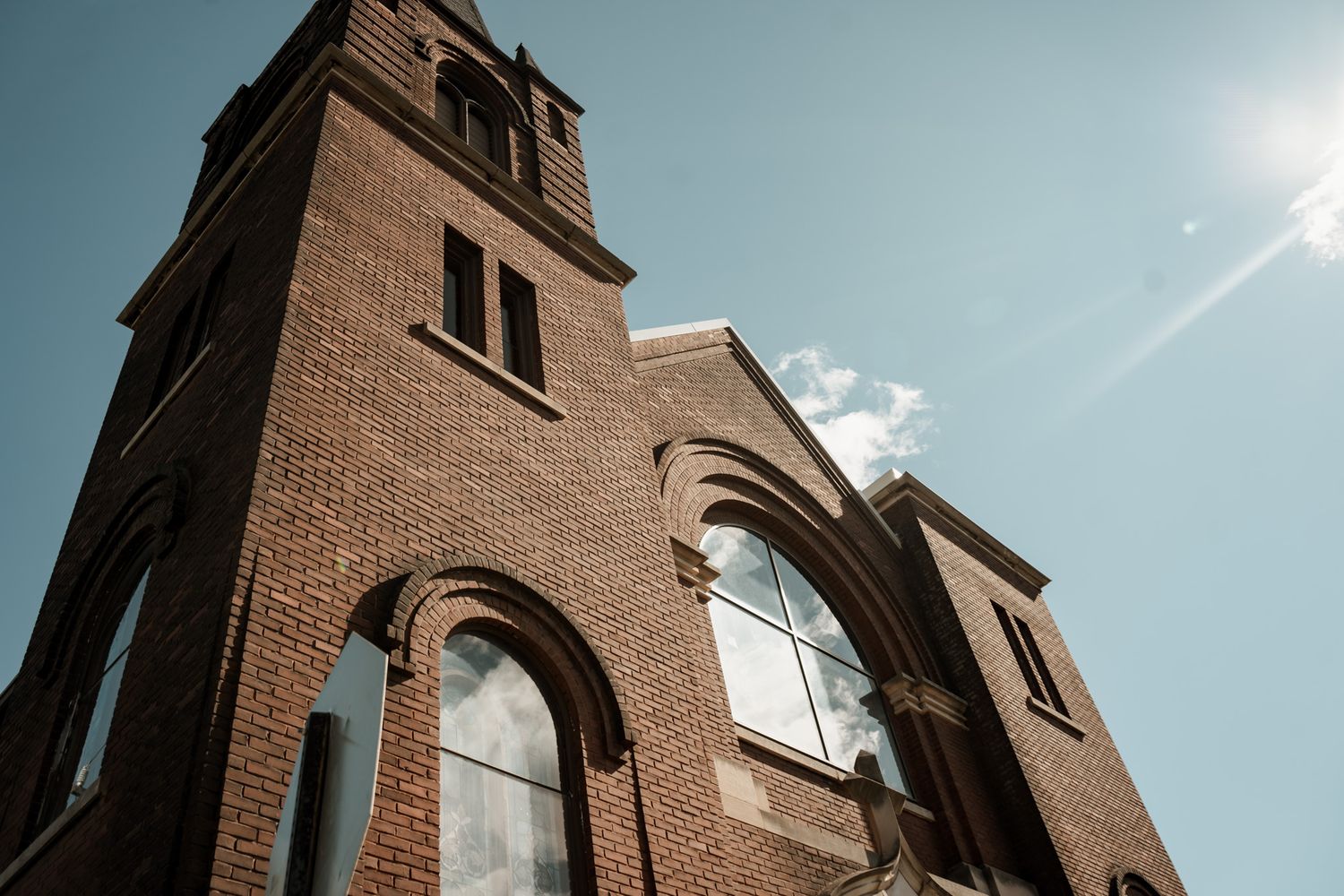 Exterior view of a traditional brick church with steeple against a bright blue sky.