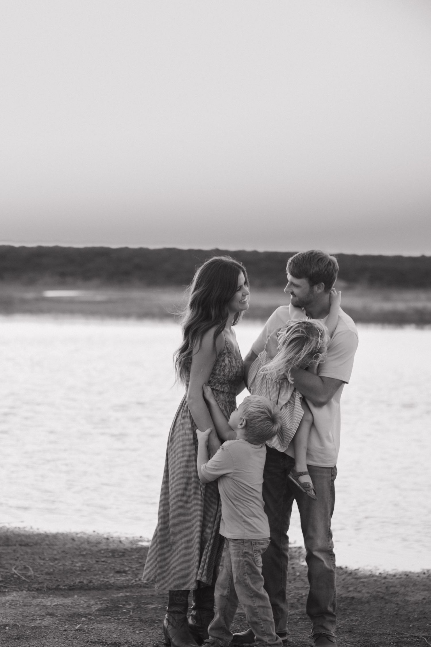 Black and white family portrait by the water at sunset.