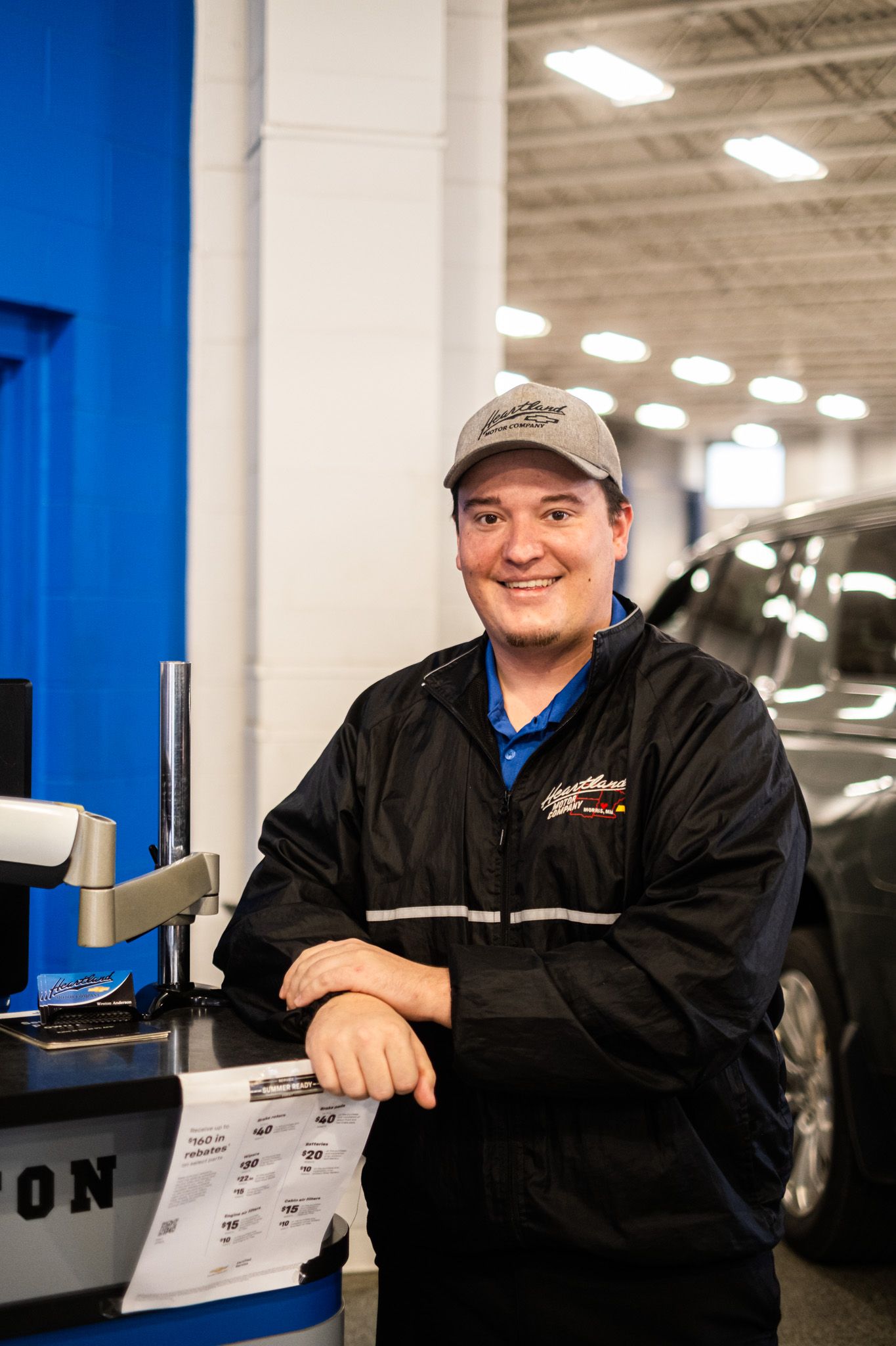 Staff member in black jacket and blue shirt reviewing paperwork at dealership desk.