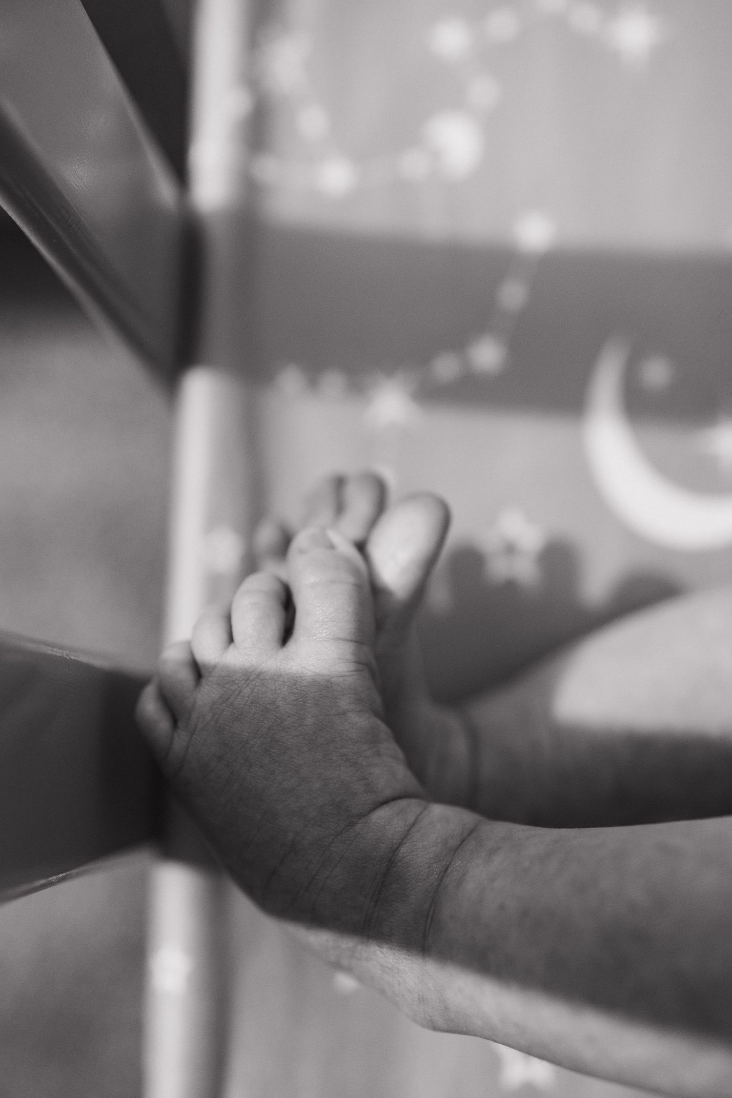 Black and white image of tiny baby feet with string lights in background.