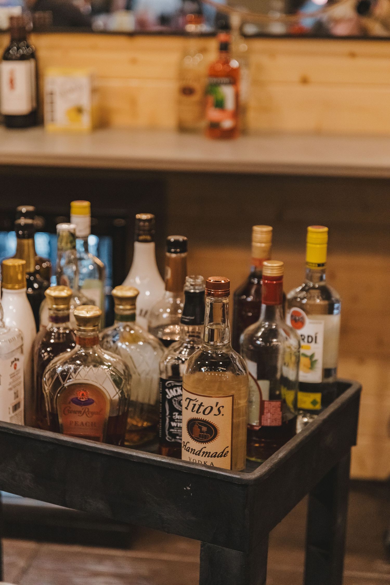Assorted liquor bottles including Tito's and Jack Daniels arranged on a black tray at a wedding bar.
