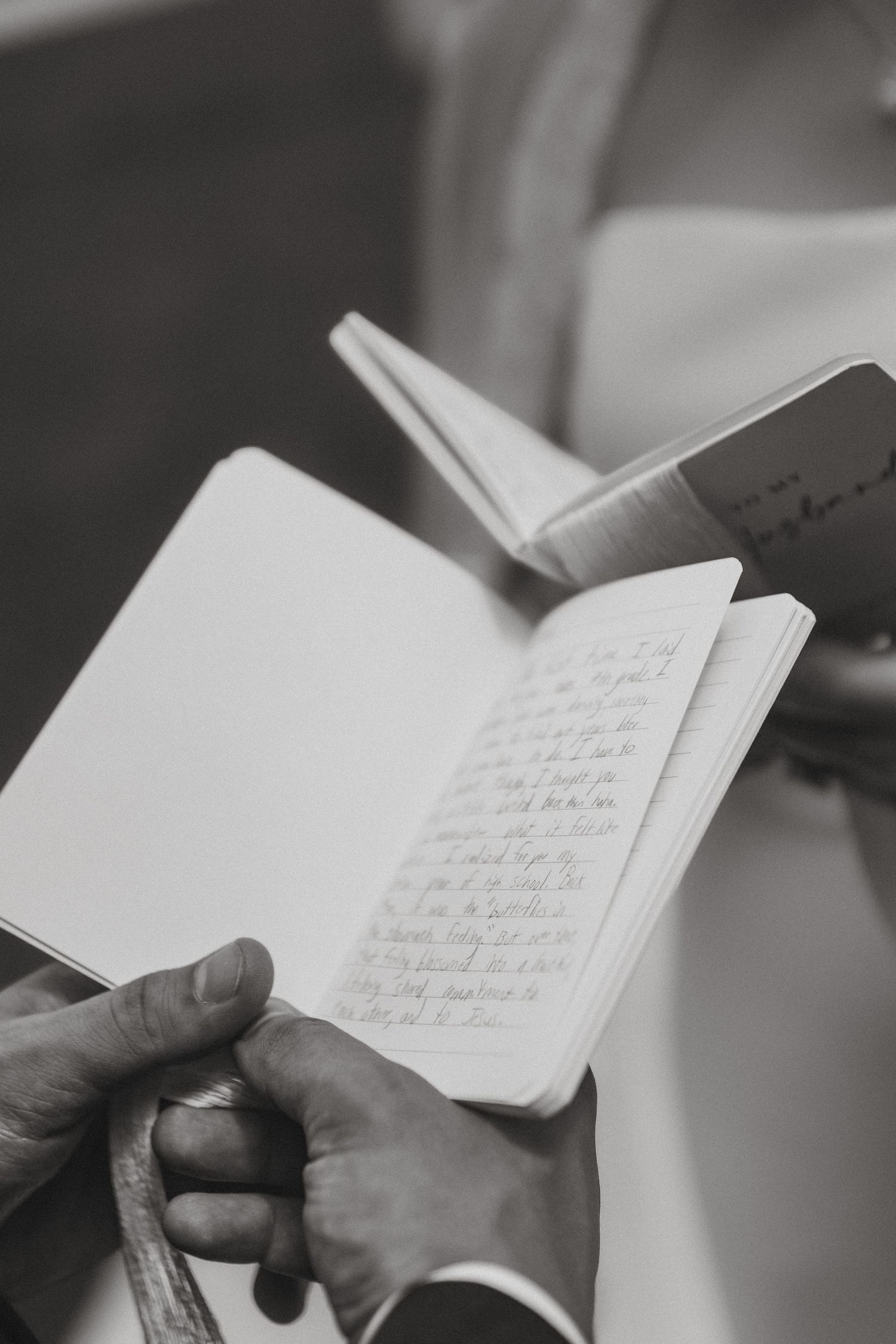 Close-up black and white photo of hands holding open journal with handwritten wedding vows.