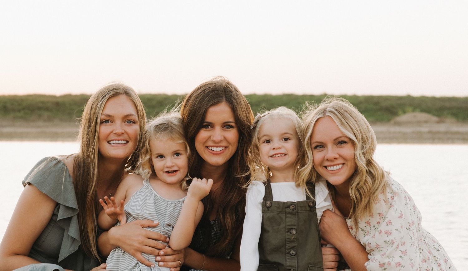 Group of people in coordinated outfits smiling together during golden hour at a lakeside.