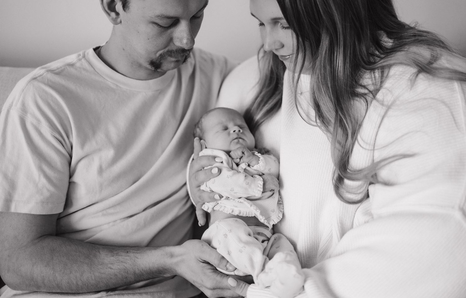 Black and white photo of new parents lovingly cradling their newborn baby together.