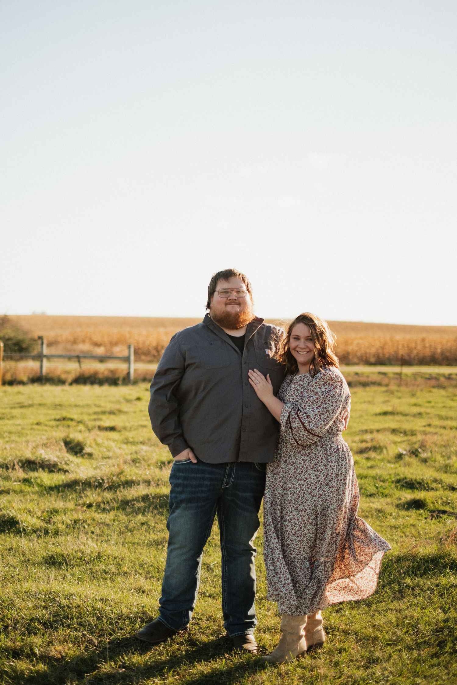 A couple poses together in a sunny field at sunset.